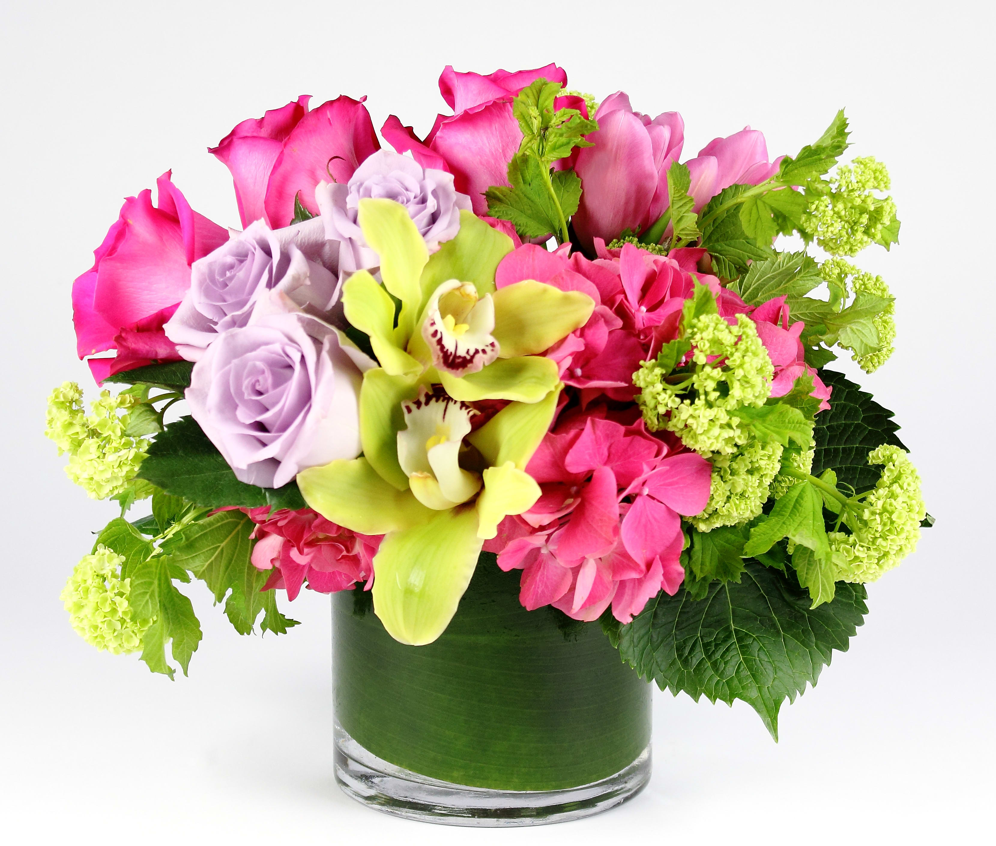 Pink roses and orchids in a glass vase with green accents
