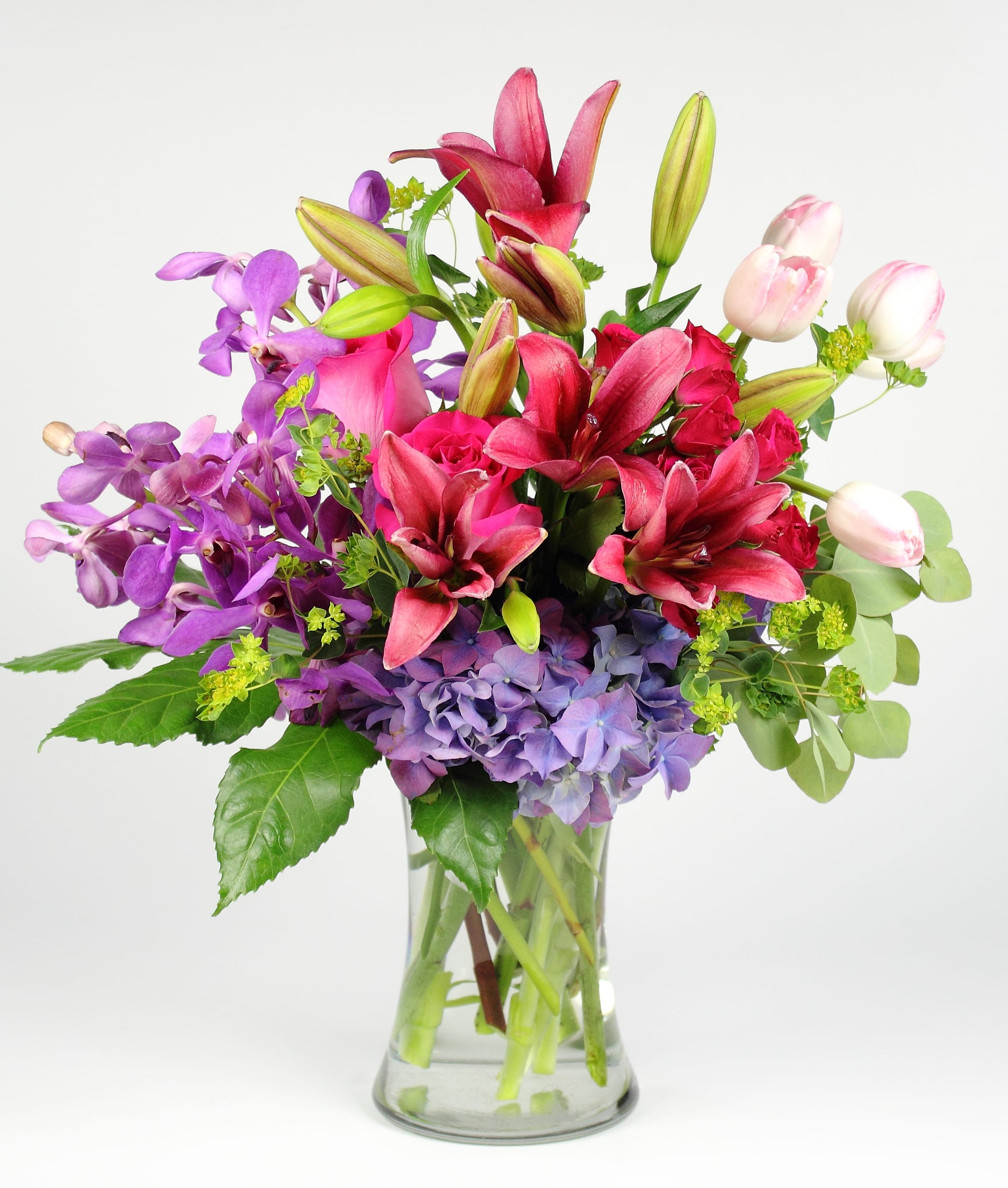 Mixed bouquet of pink lilies, purple orchids, and lavender hydrangeas in a glass vase