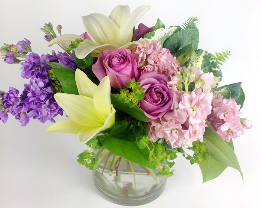 Bouquet of pink roses, lilies, and purple flowers in a glass vase