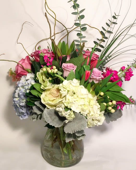 Mixed bouquet of pink roses, hydrangeas, and white blooms in a glass vase