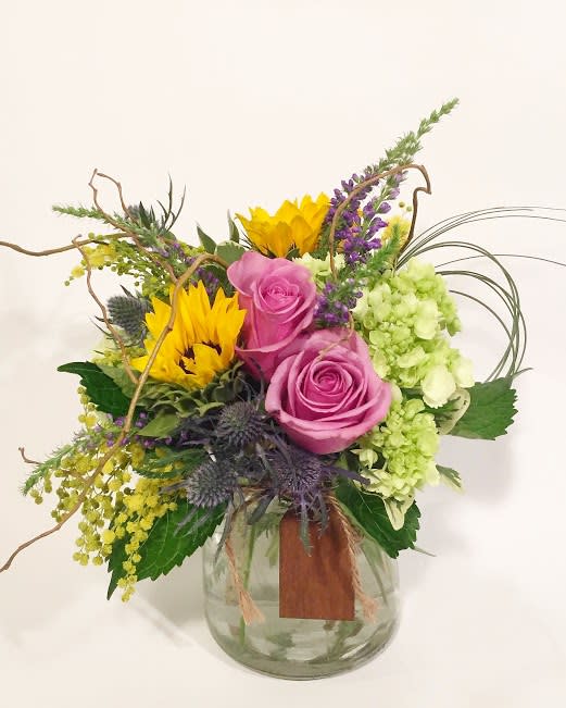 Mixed bouquet with pink roses, sunflowers, and green hydrangea in a glass vase