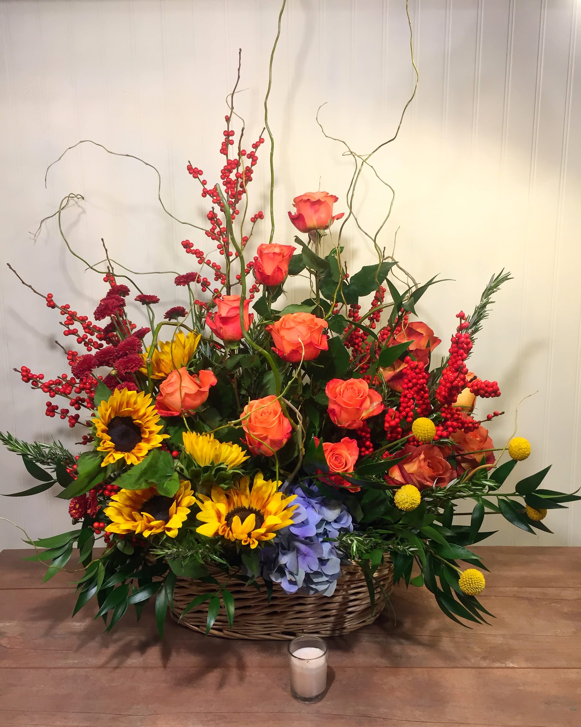Basket arrangement of roses, sunflowers, and berries with tall curly branches