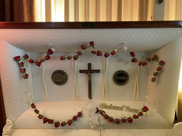 White casket with red rose garland and a crucifix inside