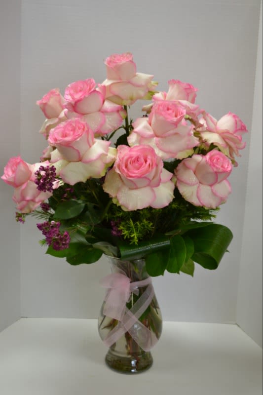 Pink-tipped roses arranged in a clear glass vase with a pink ribbon
