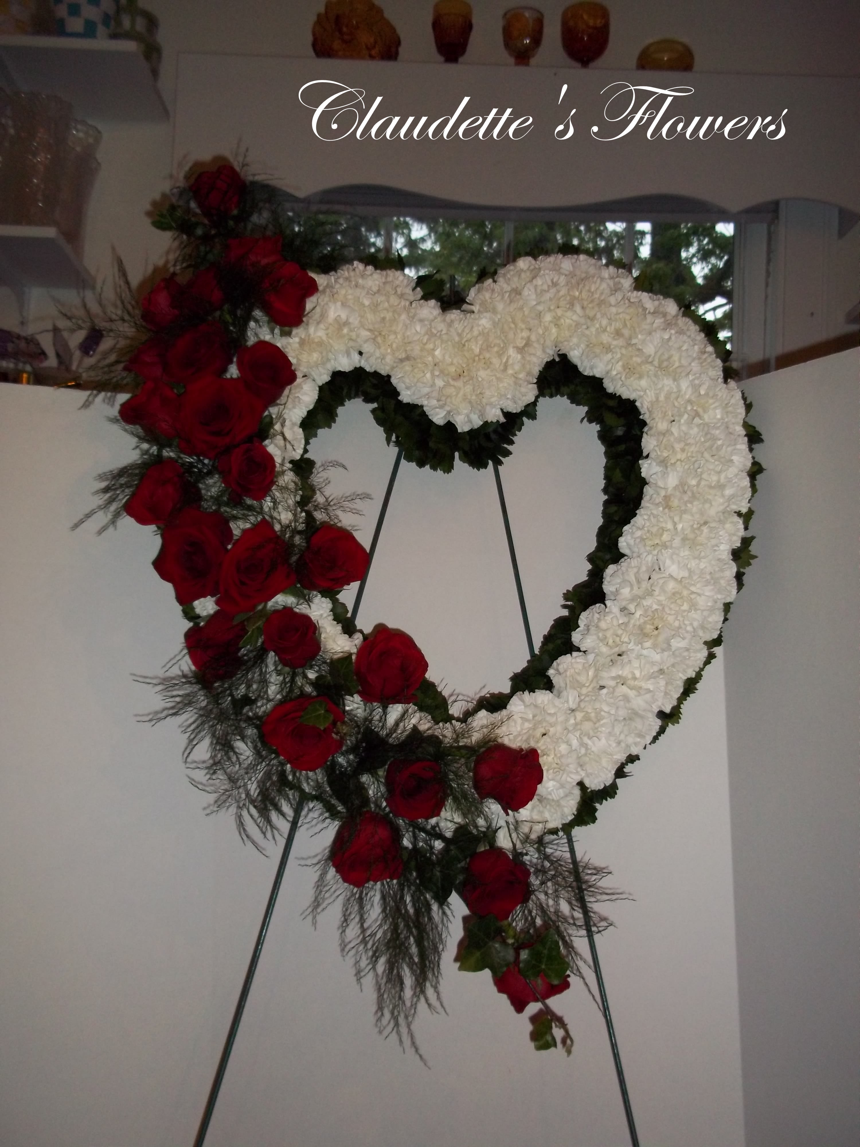 Heart-shaped floral wreath with red roses and white flowers on an easel