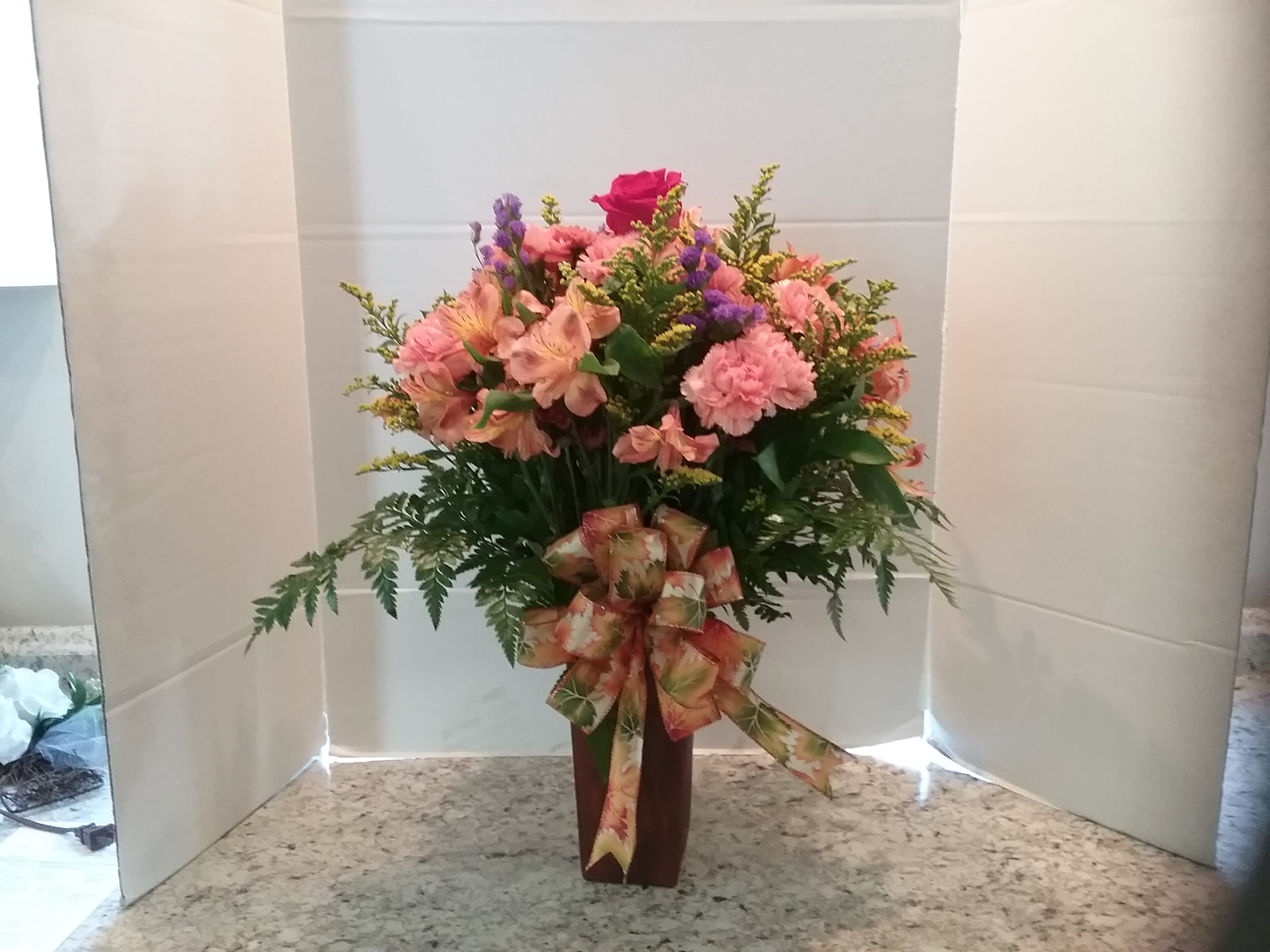 Pink and peach mixed flower arrangement in a tall vase with a ribbon