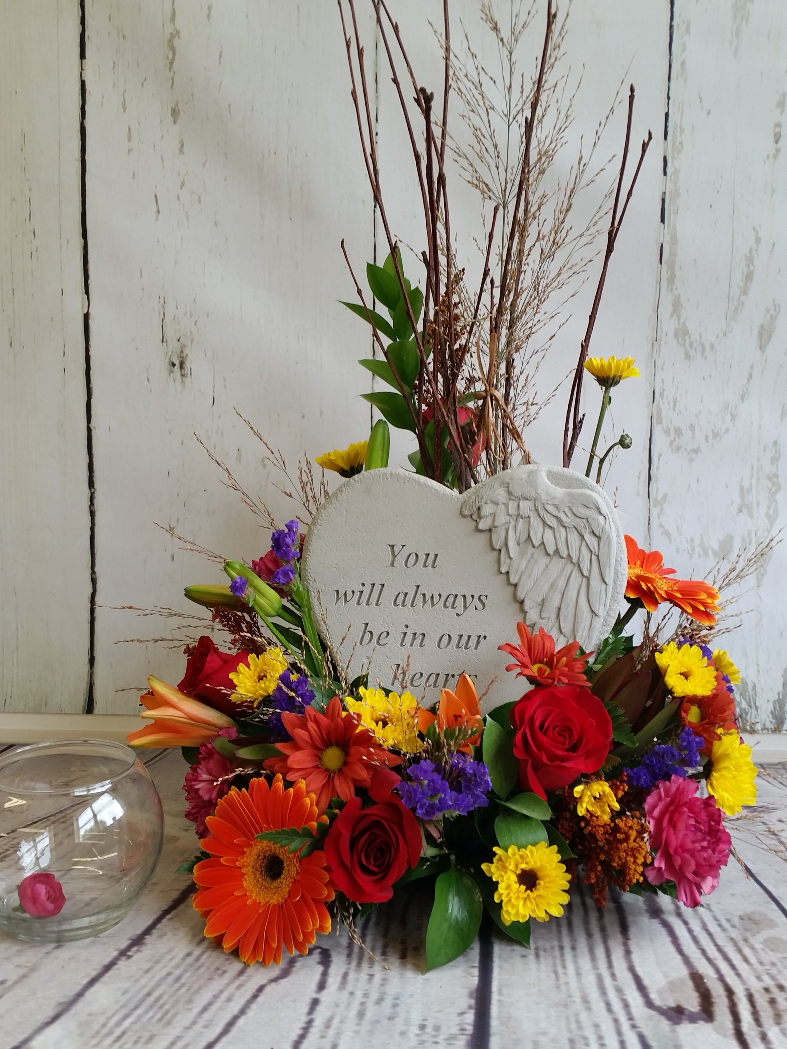 Heart-shaped memorial plaque surrounded by colorful flowers and a glass candle holder