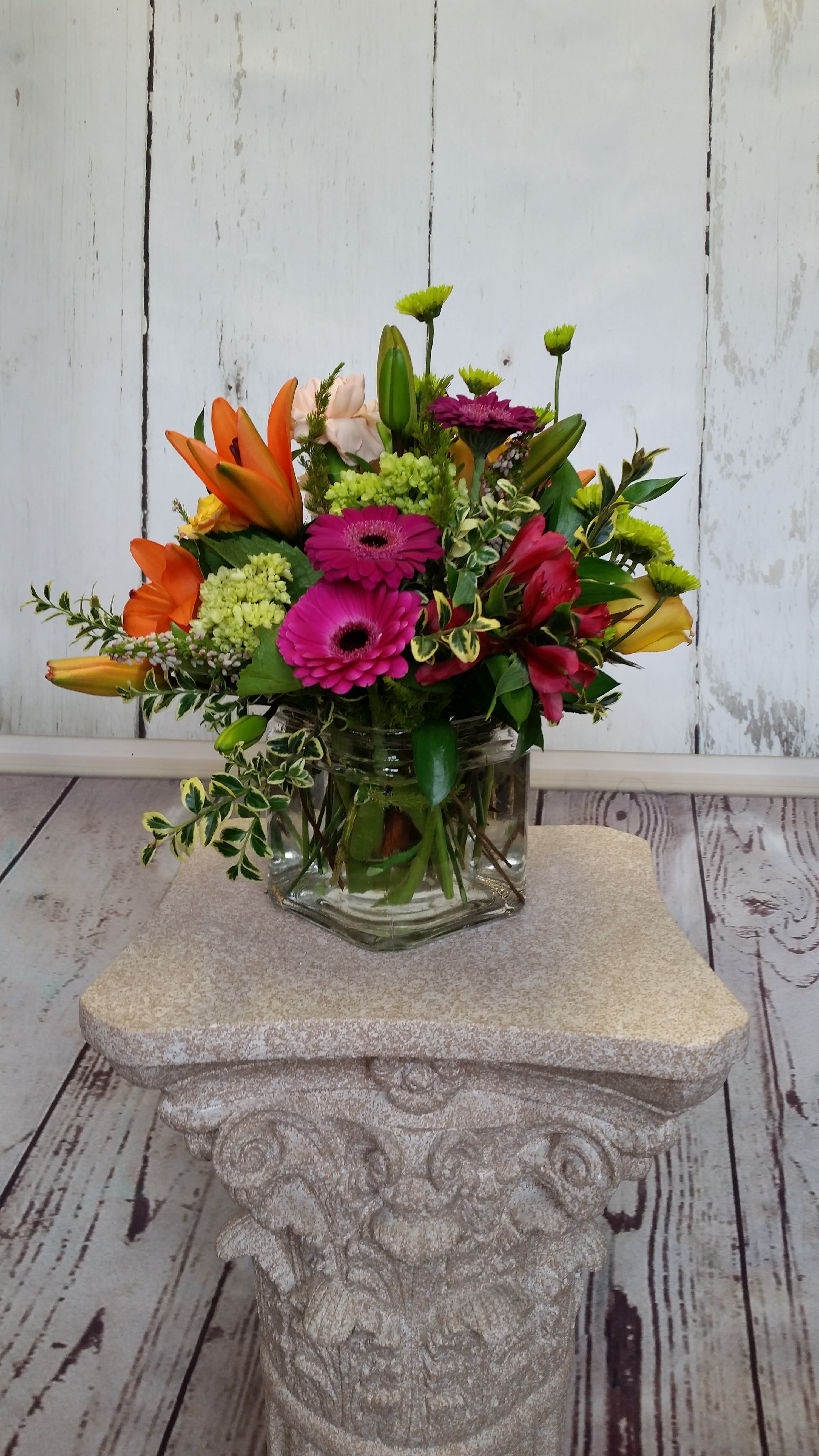 Mixed bouquet of orange lilies, pink gerbera daisies, and green mums in a glass vase