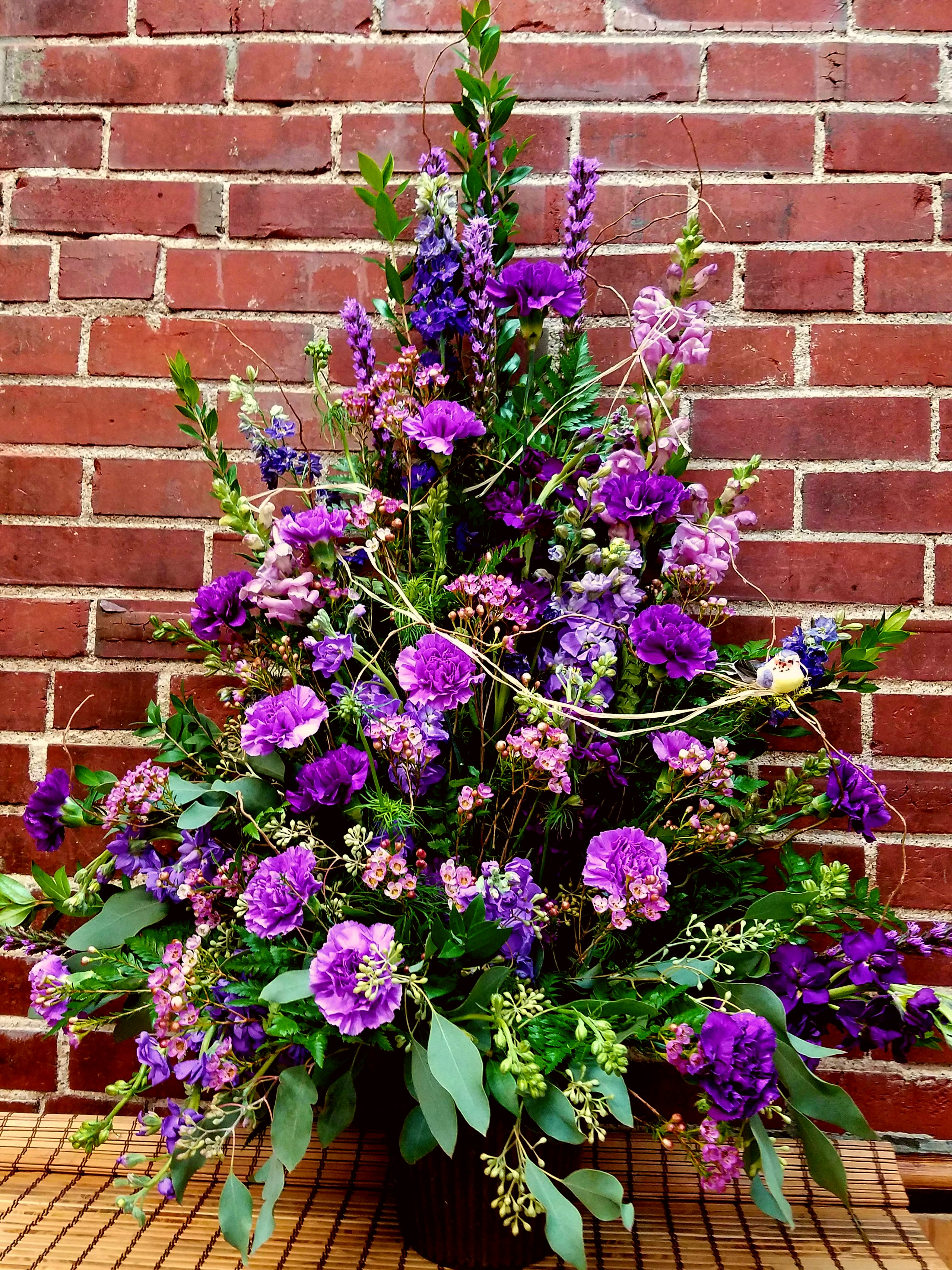 Tall purple floral arrangement in a dark vase