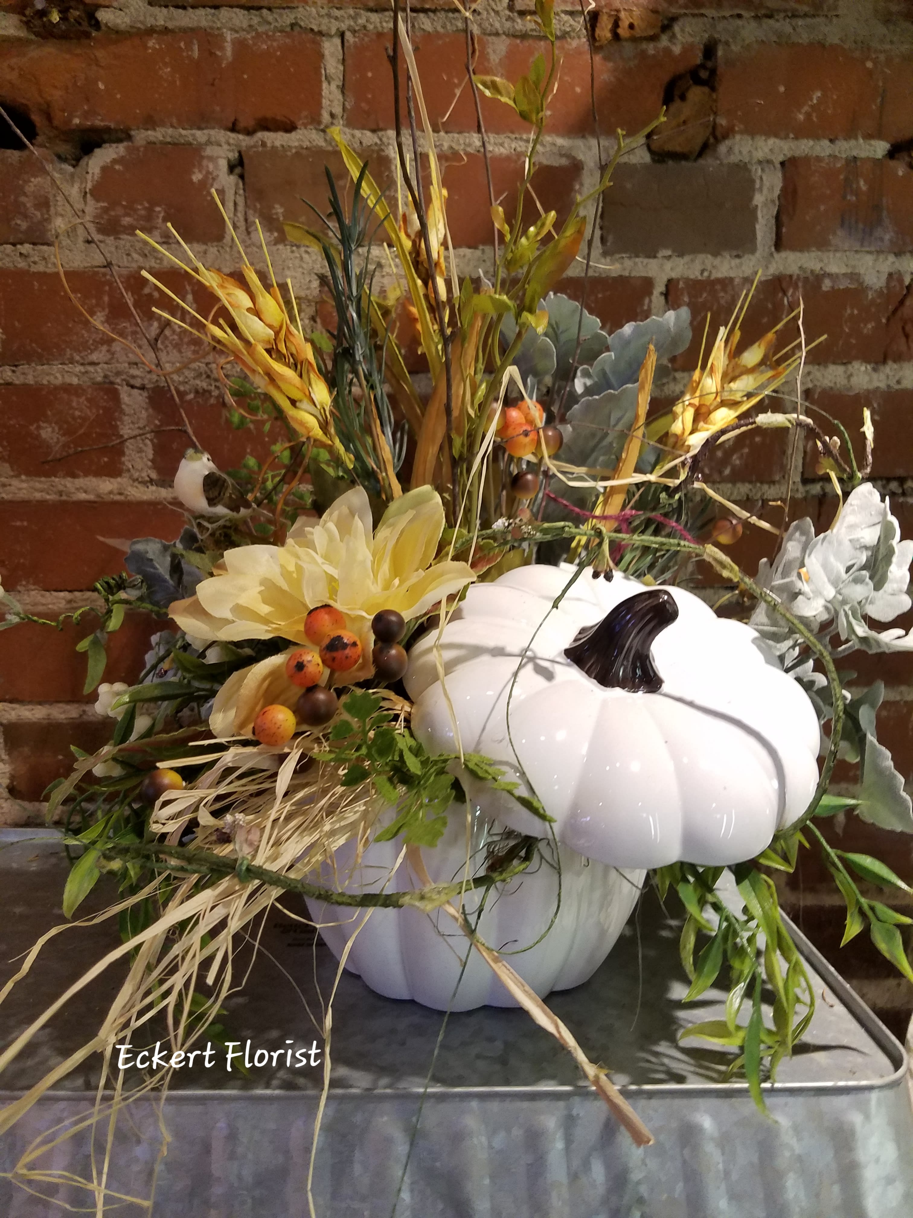 Eckert Florist's Permanent Botanical White Pumpkin *LOCAL DELIVERY ONLY - This white ceramic pumpkin is filled with artificial neutral colored flowers and greens. A non-typical autumn choice for that someone special or for your own decor. *Flowers and colors may vary.   
