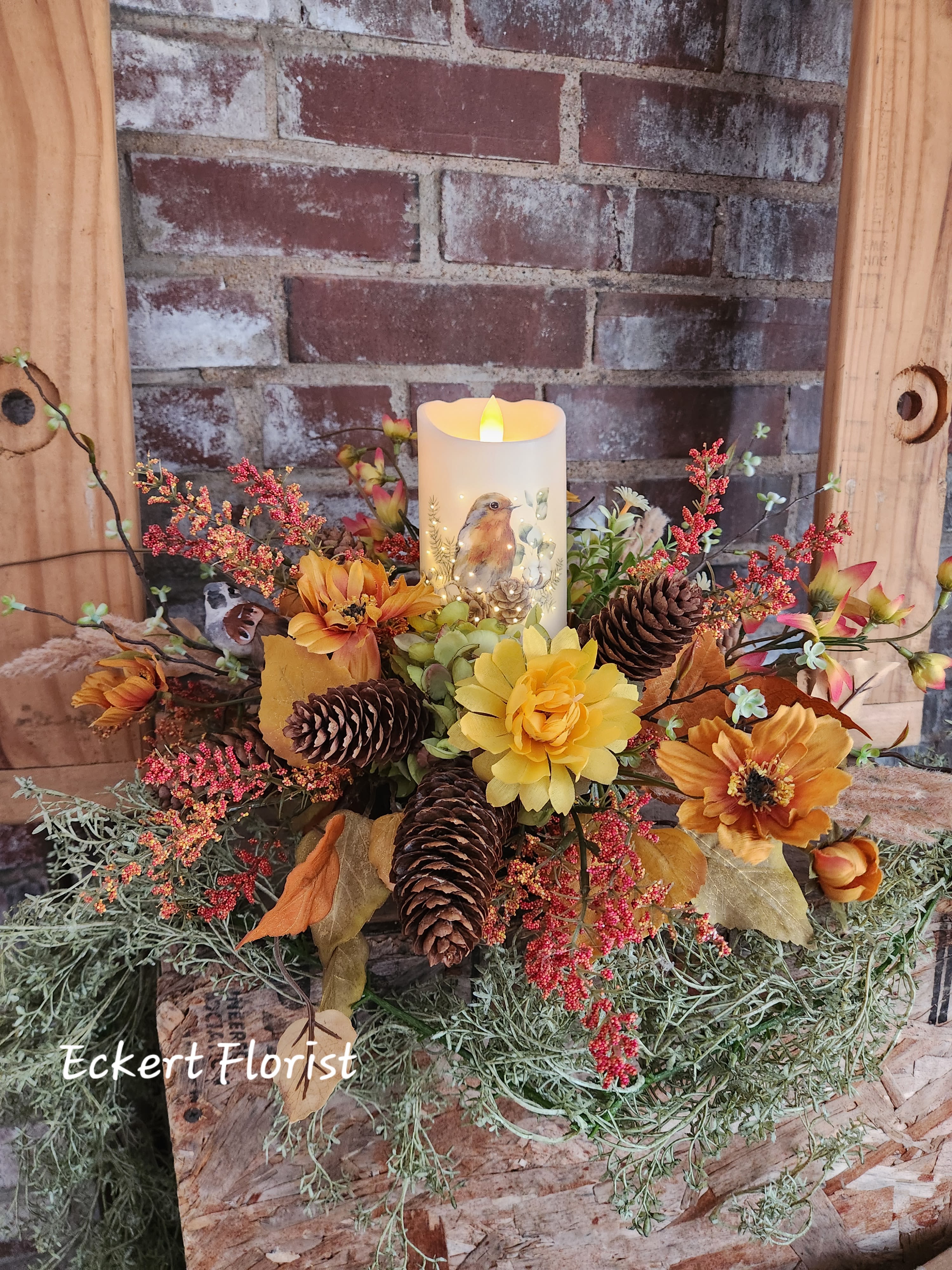 Eckert Florist's Bird Candle Artificial Centerpiece *Our  Local Delivery Only - Created in a ceramic design bowl, this artificial autumn colored centerpiece features a battery powered illuminated bird motif candle, perfect for any home decor! Approx. 19" wide x 10" High *2 AA Batteries included *Our local delivery only