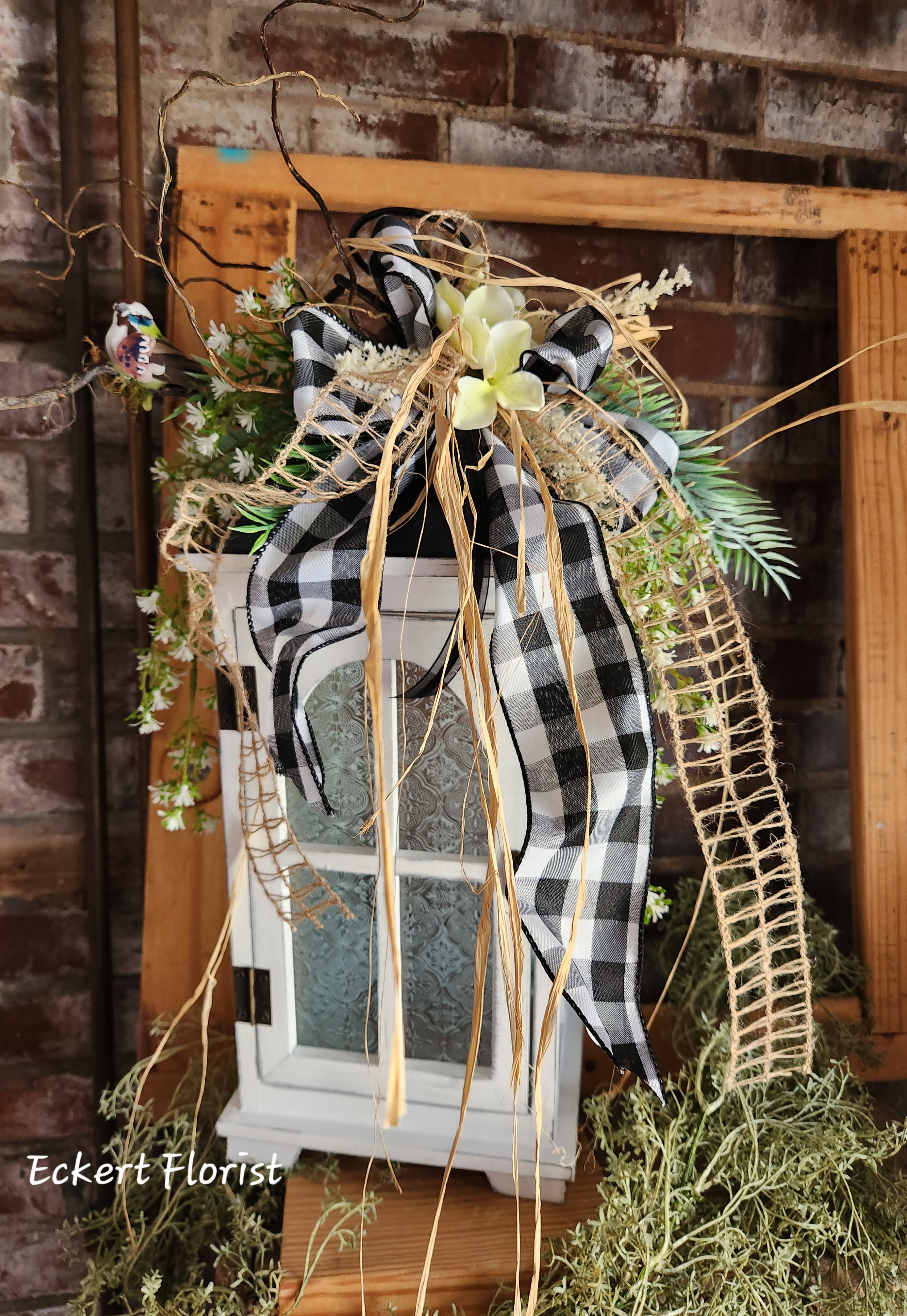 Decorative floral arrangement on a white lantern with black plaid ribbon