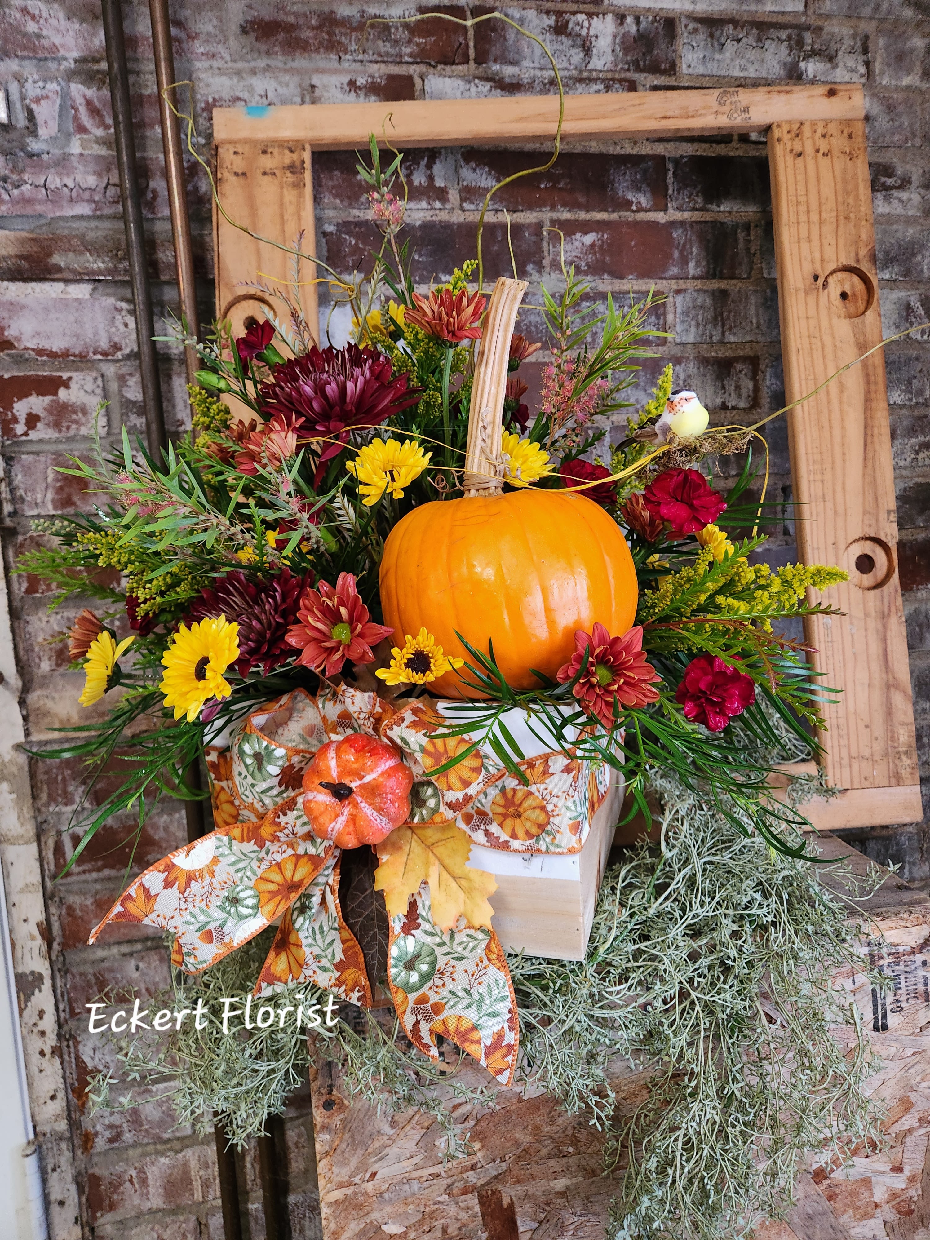 Eckert Florist's Pumpkin Patch Bouquet *Our Local Delivery Only - This 9.5" square by 6" high wooded crate decorated for fall,  is filled with this seasons finest fresh flowers. A real pumpkin is included along with our signature willow and faux bird to complete the look. *Our Local Delivery Only 