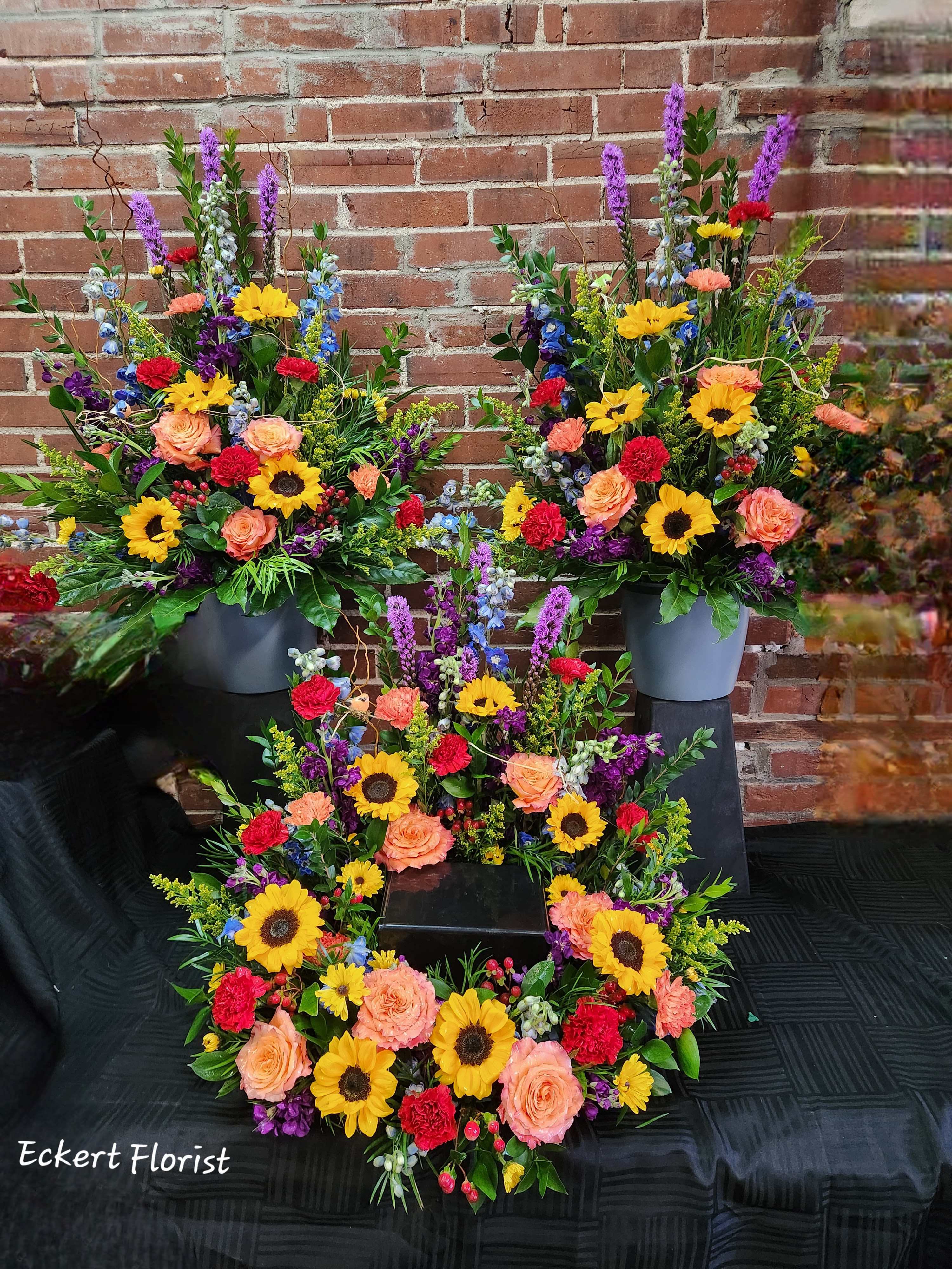 Eckert Florist's Bright Memorial Urn Arrangement (Photo Represents Premium Upgrade) *Our Local Delivery Only - This 3-piece arrangement set (Premium) is perfect for any memorial service. Made with the season's most beautiful bright blooms, an urn or picture may be placed in the center of the round floral piece. *Flower variety and colors may vary *Urn not included. *STANDARD: Includes "1" Round Urn Arrangement Only *DELUXE: Includes "1" Round Urn Arrangement and "1" Coordinating Side Piece *PREMIUM: Includes "1" Round Urn Arrangement and "2" Coordinating Side Pieces *Our local delivery only