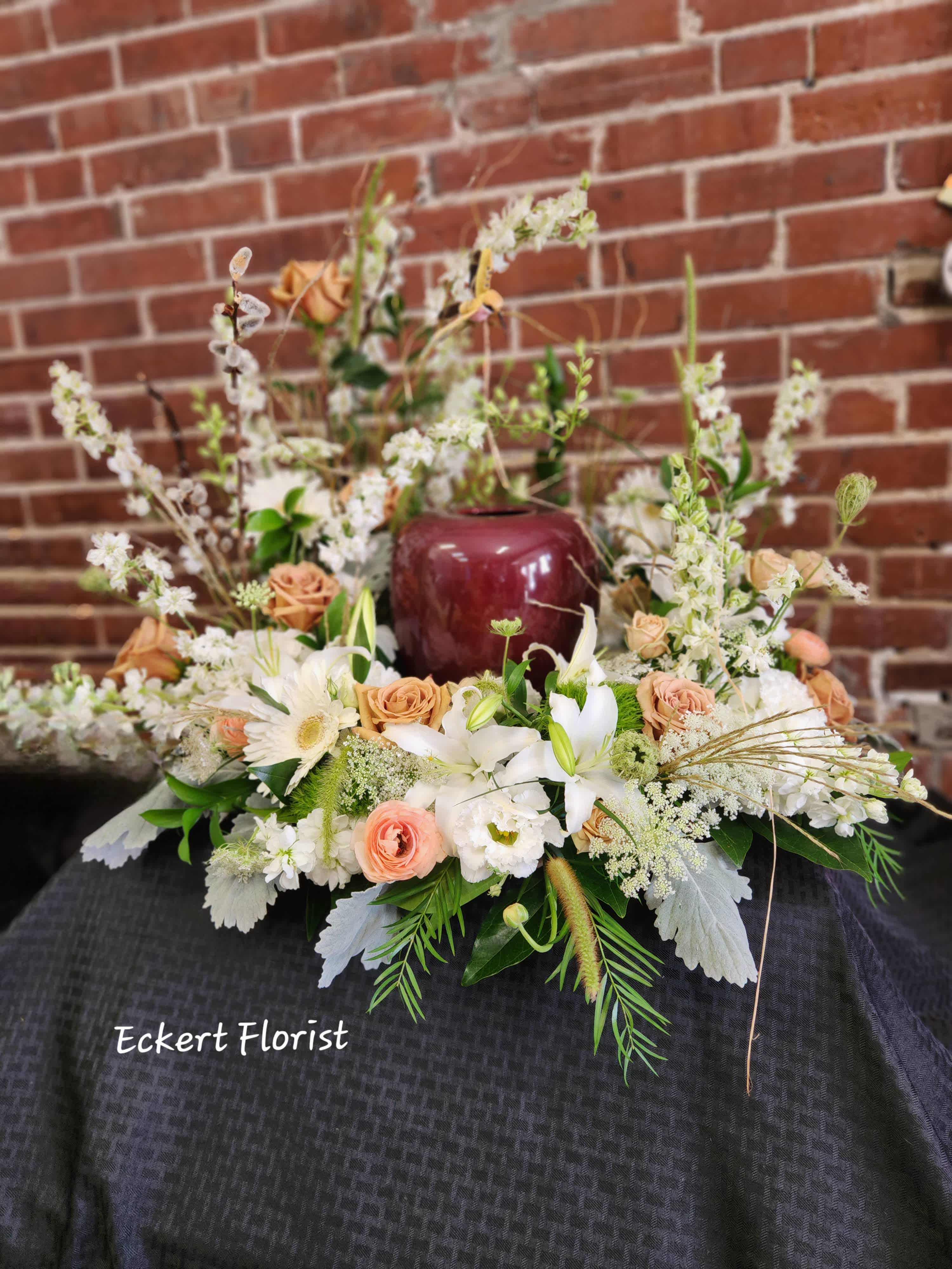 Low floral arrangement with white lilies, peach roses, and white daisies in a burgundy vase