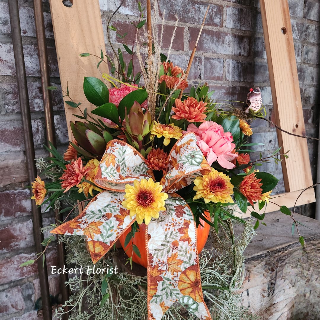 Autumn floral arrangement in an orange container with a patterned bow