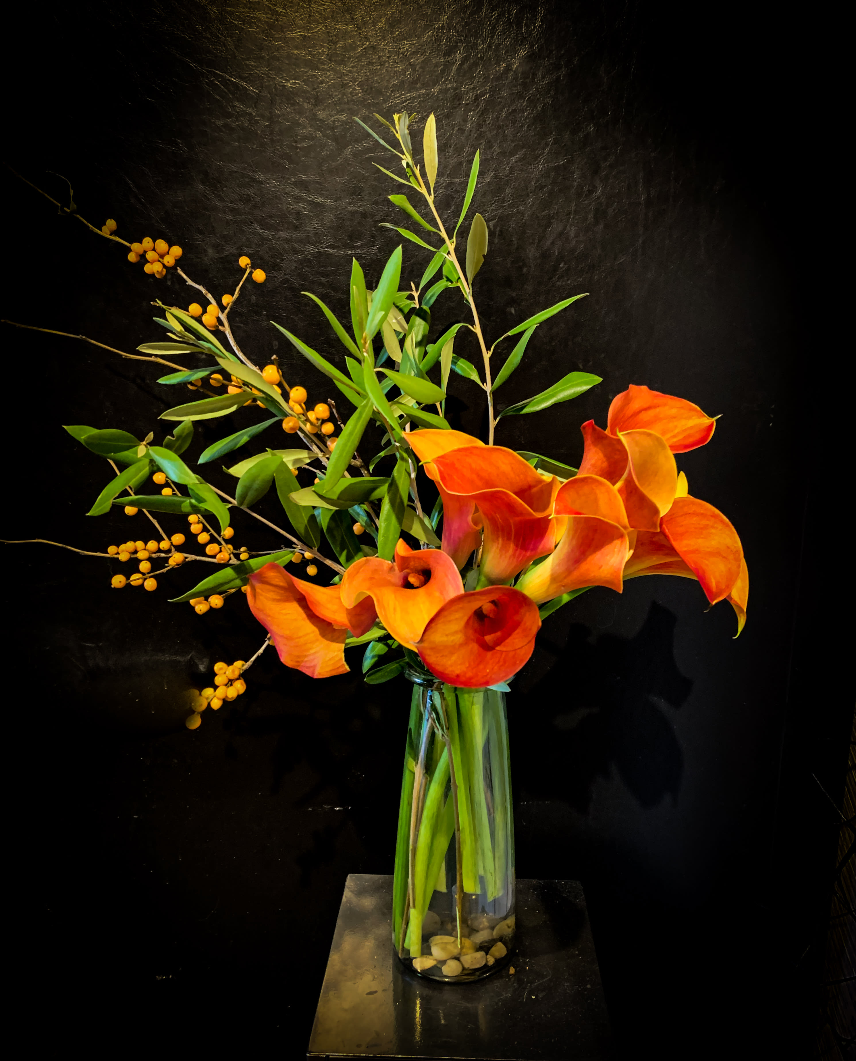 Modern Sunset Mini Callas in vase  - Clean and striking, a dozen sunset mini calls are grouped together in a tall thin vase accent with greenery and some berries.  Approx 16" tall. 