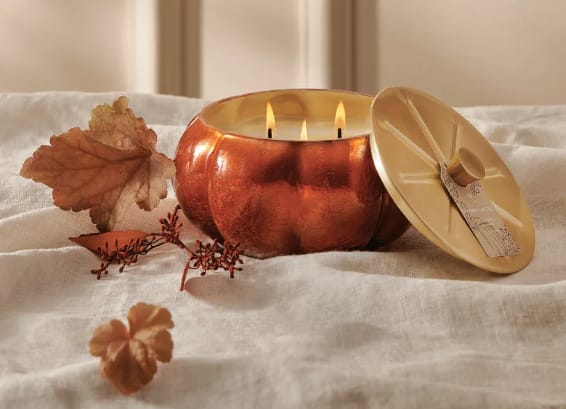 Copper candle with lid and autumn leaves on a white fabric surface