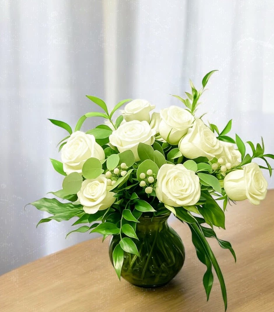White roses arranged in a green glass vase with lush foliage