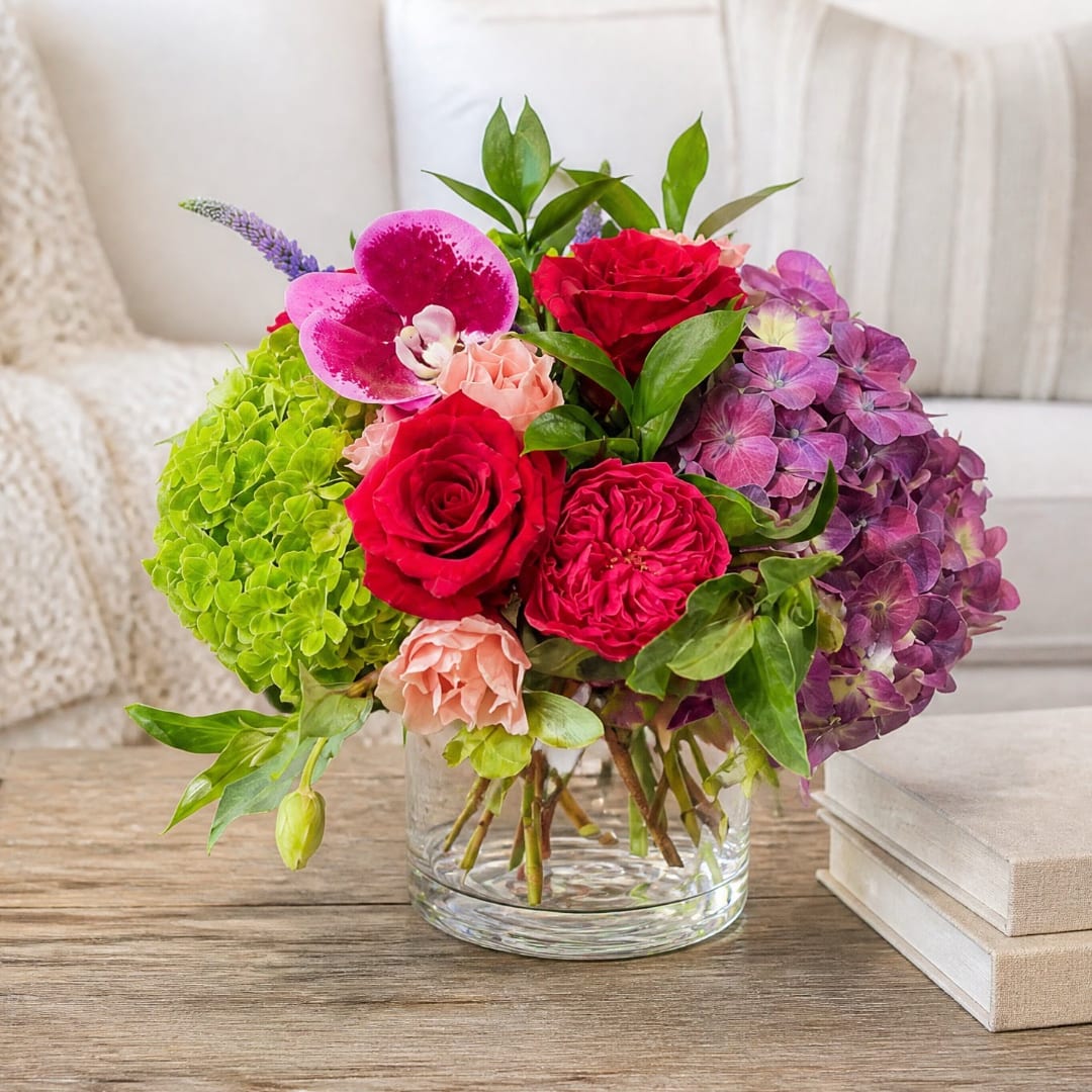 Colorful bouquet of roses, hydrangeas, and orchids in a clear glass vase