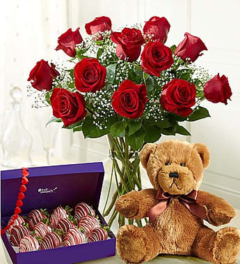 Red roses in a glass vase with a teddy bear and a box of chocolate-covered strawberries