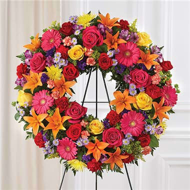 Colorful floral wreath on a black stand with roses and daisies