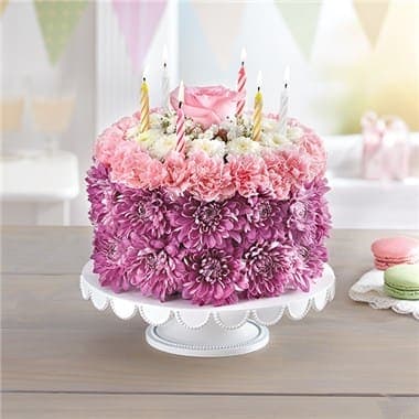 Pink and purple flower-covered cake with birthday candles on a white stand