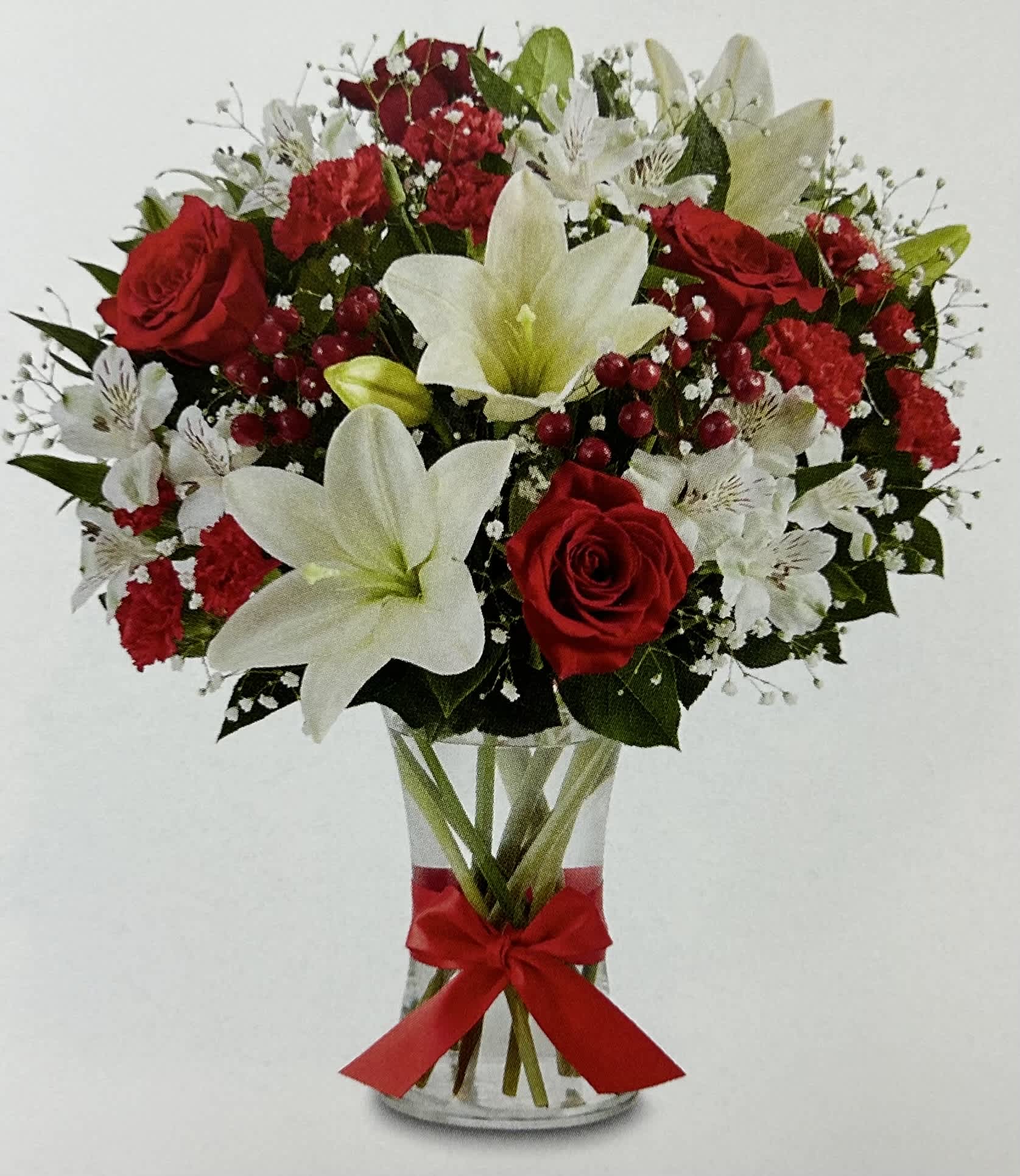 Red roses and white lilies in a clear glass vase with a red ribbon