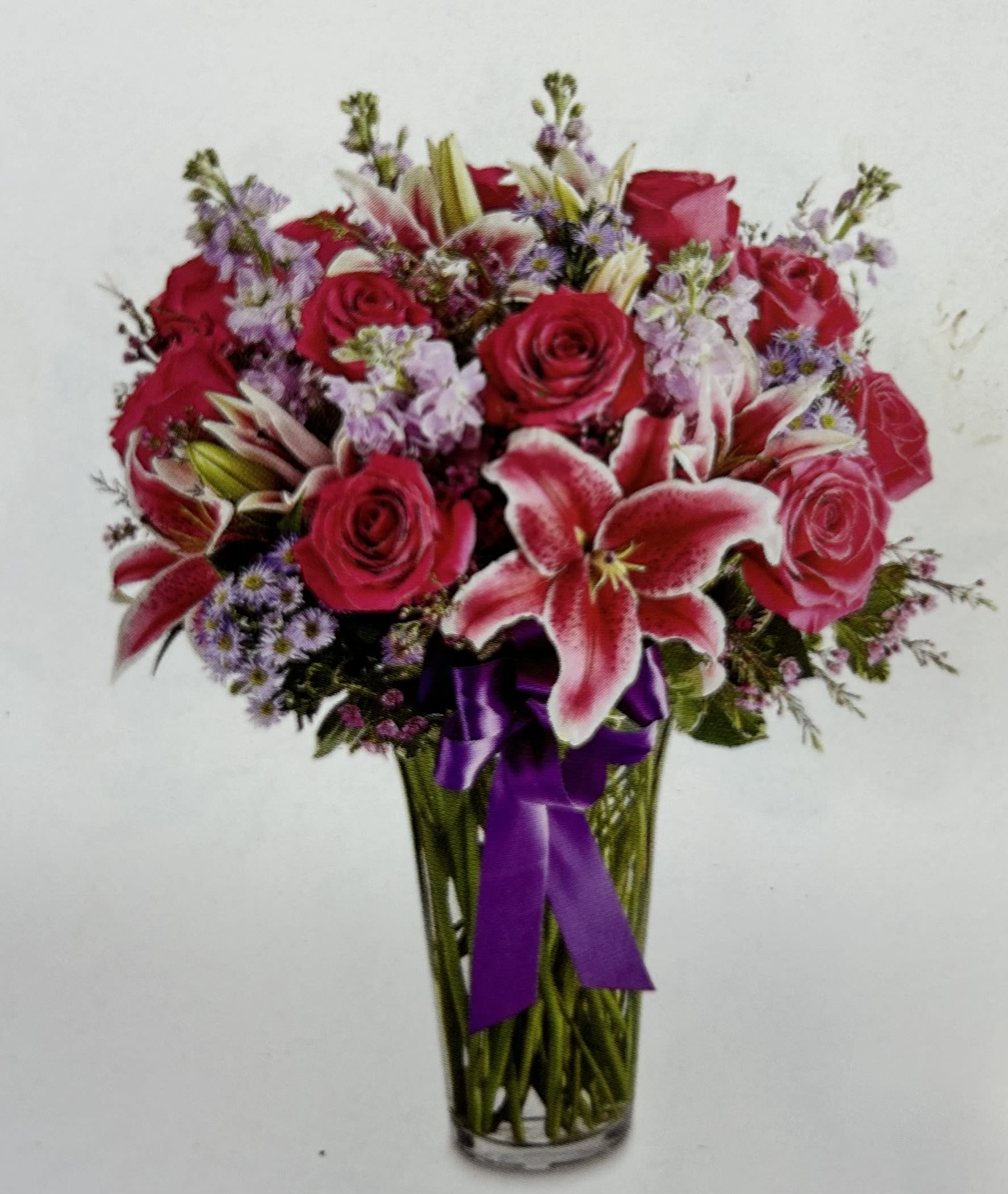 Bouquet of red roses and pink lilies in a glass vase with a purple ribbon