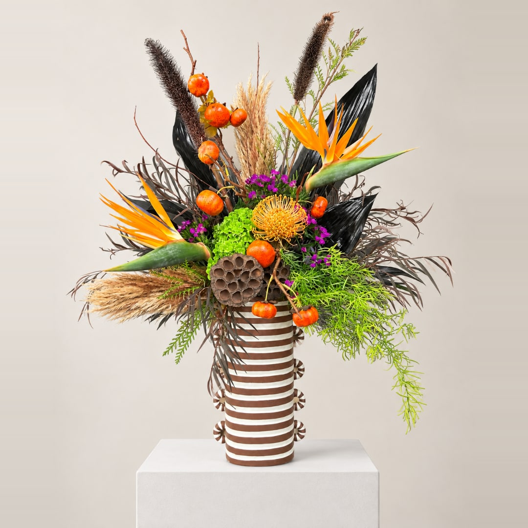Tropical arrangement with orange bird-of-paradise in a striped vase