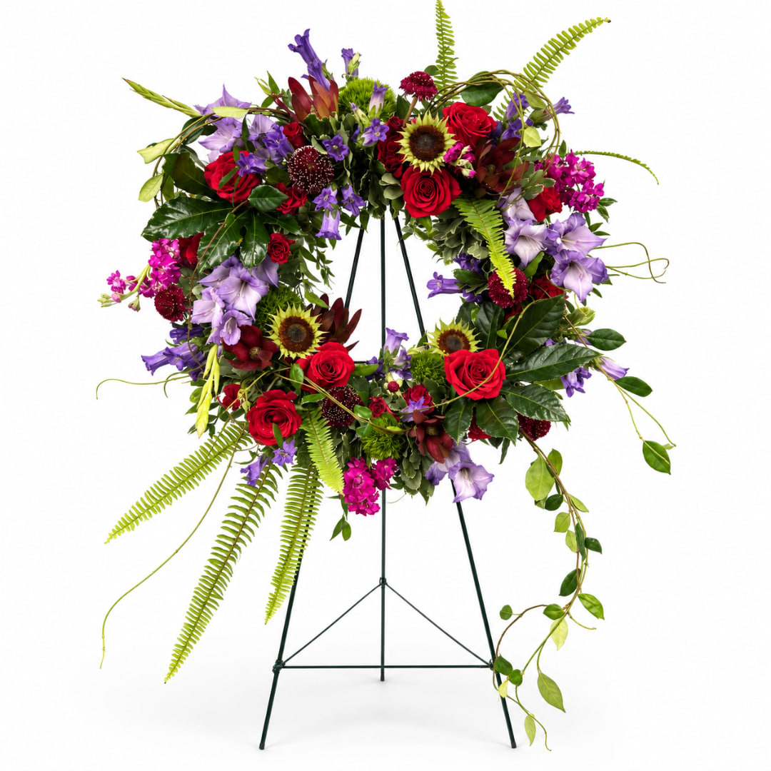 Circular floral wreath on a metal stand with red, purple, and pink flowers