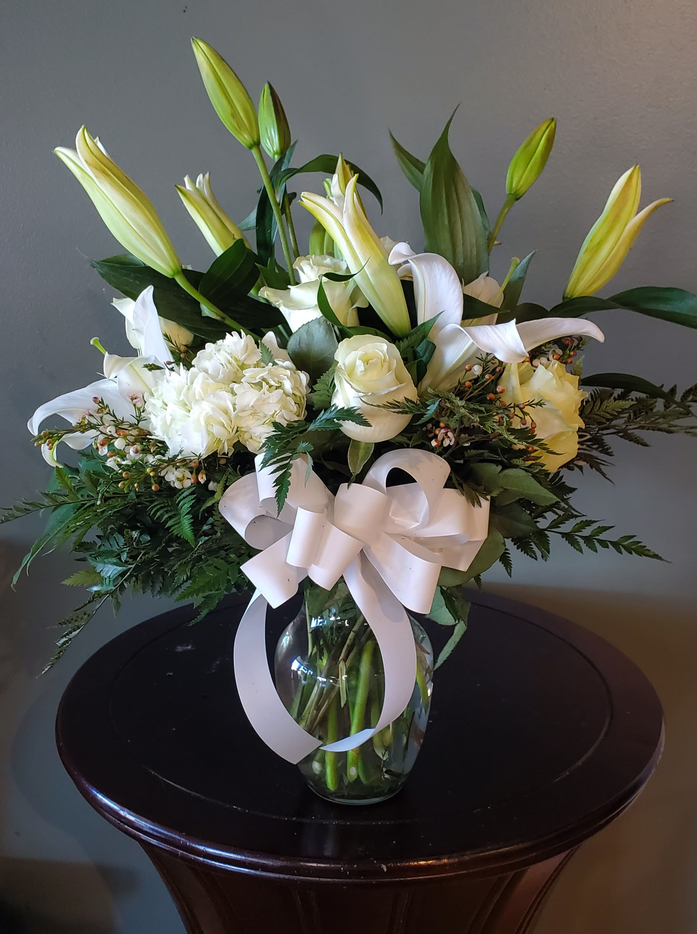 White lilies and roses arranged in a glass vase with a white ribbon