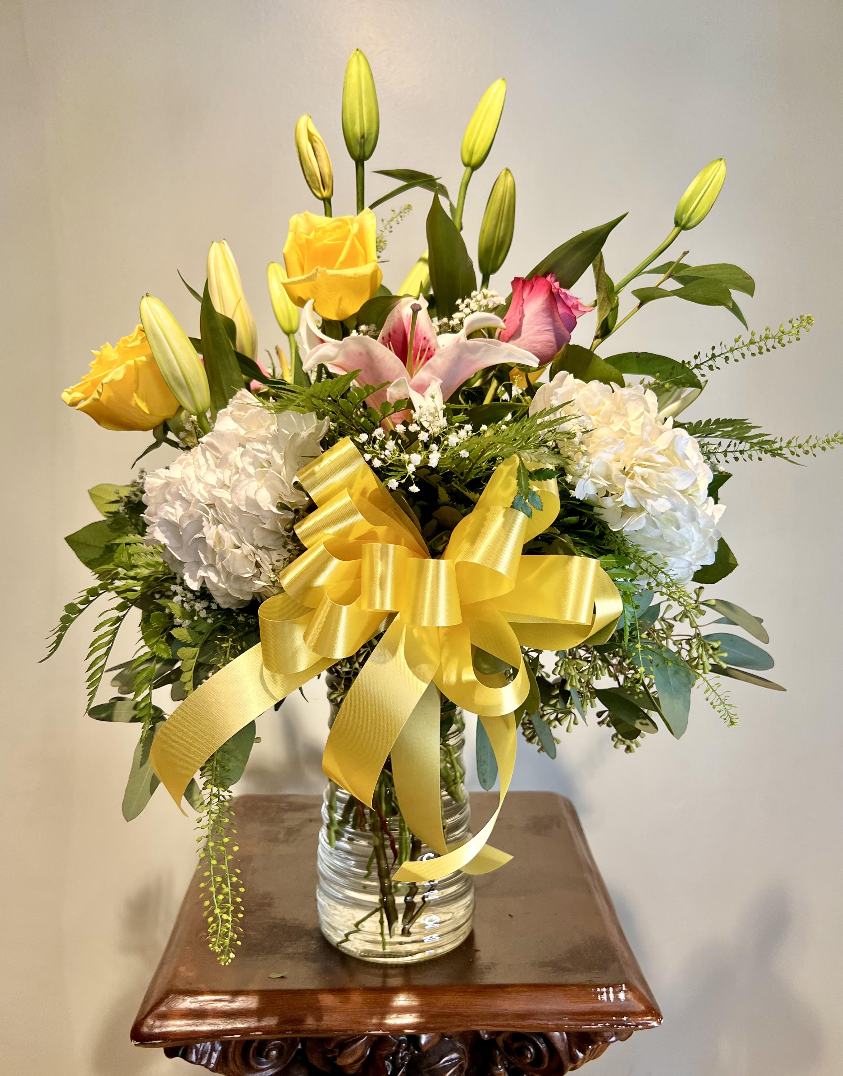 Bouquet of yellow roses, lilies, and white hydrangeas in a glass vase