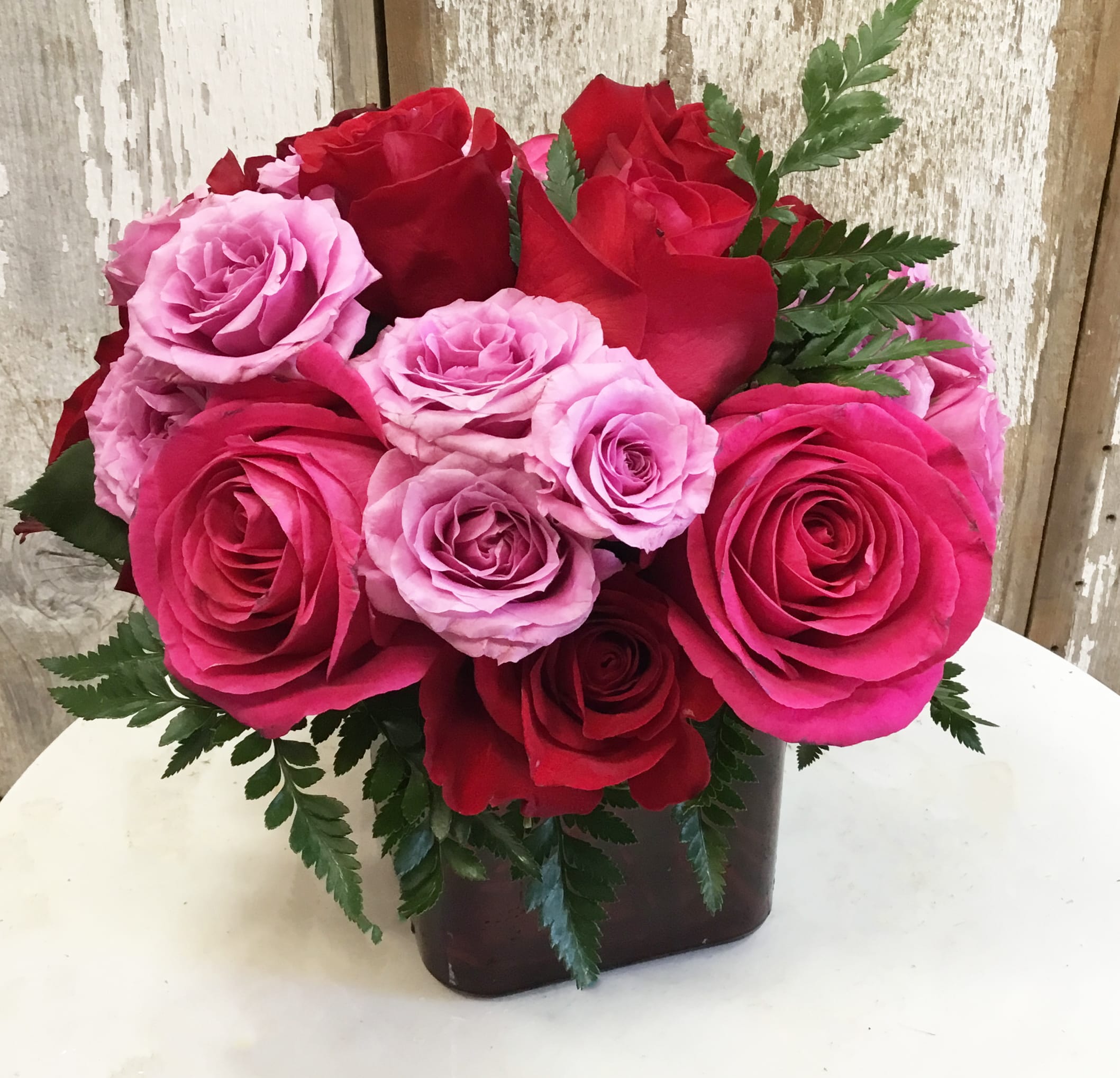 Madly in Love Bouquet with Red Roses by Teleflora - If you're crazy about someone and not afraid to show it, this bright jewel-toned arrangement is the perfect way to express your love.  Lavender, red and hot pink roses along with coral and red spray roses arranged in a red-hot cube vase are an absolutely beautiful way to get your message across.  Approximately 11" W x 10" H  Orientation: All-Around  As Shown : T9-3A Deluxe : T9-3B Premium : T9-3C