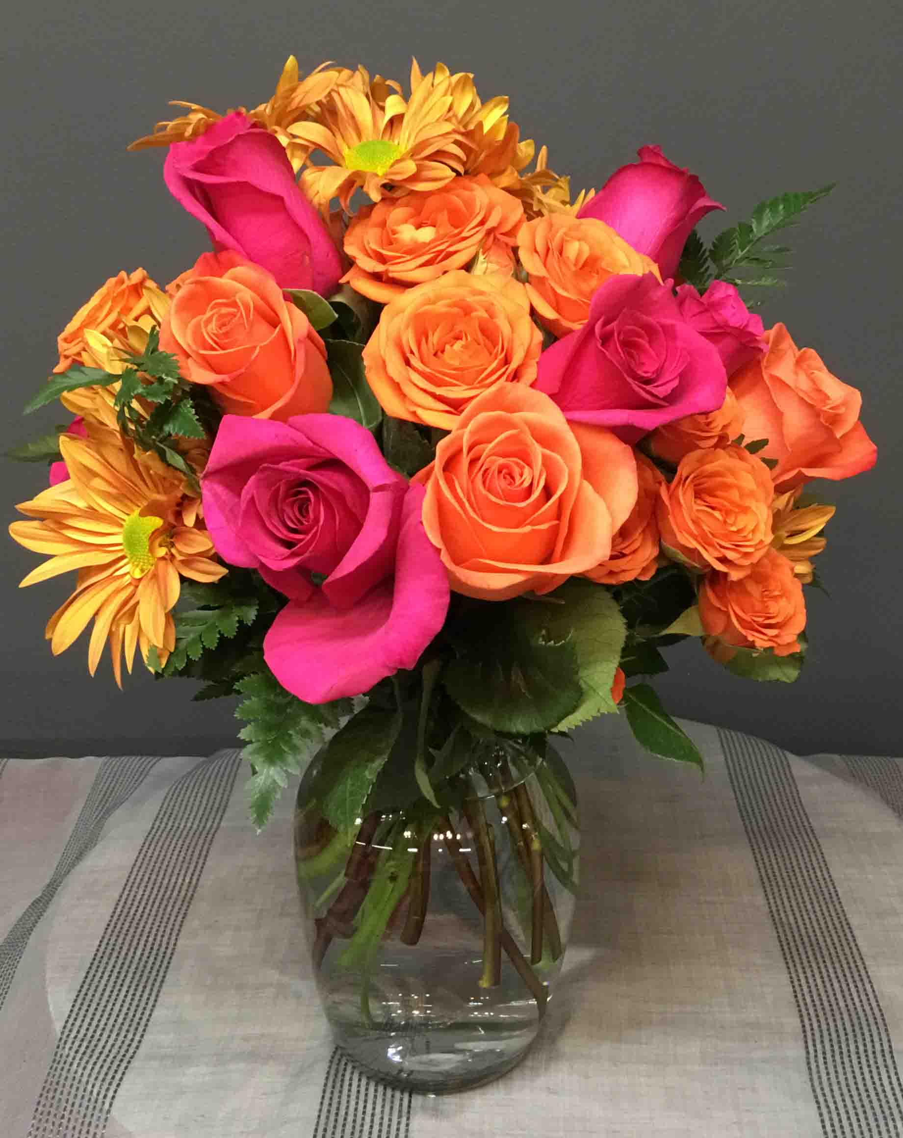 Bouquet of orange and hot pink roses with yellow daisies in a glass vase