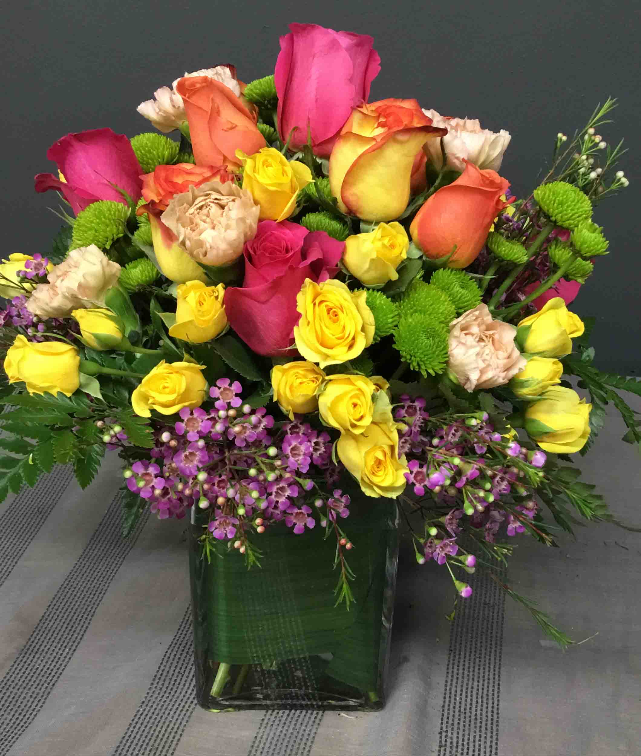 Mixed roses in a square glass vase with purple filler flowers