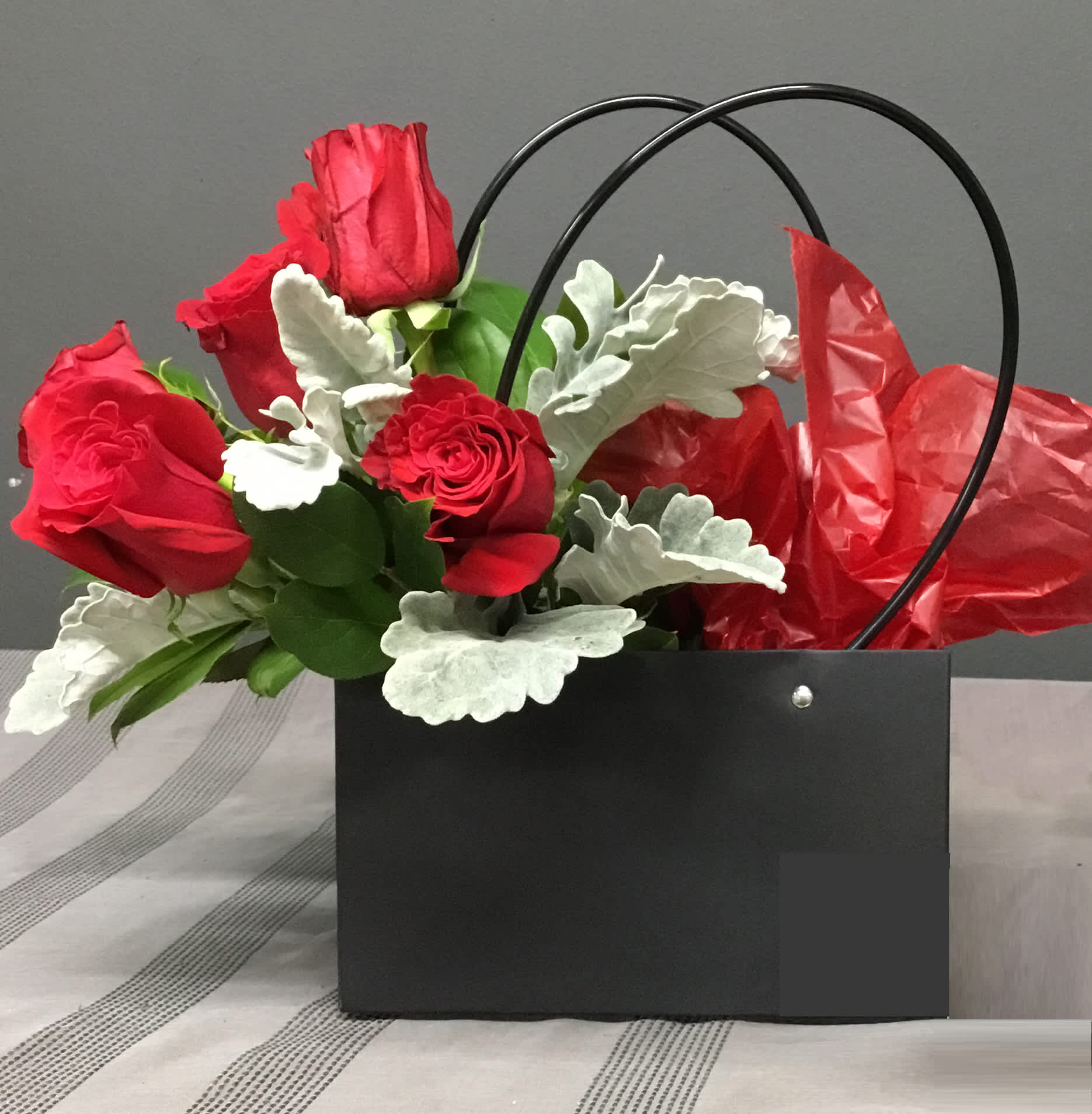 Red roses in a black gift bag with silver foliage and red tissue paper