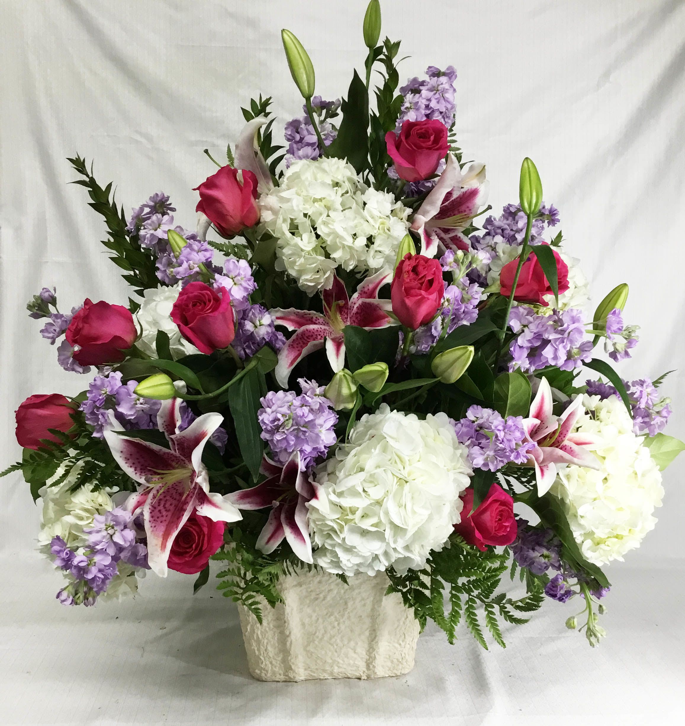 Large bouquet of pink roses, white hydrangeas, and purple lilies in a white vase