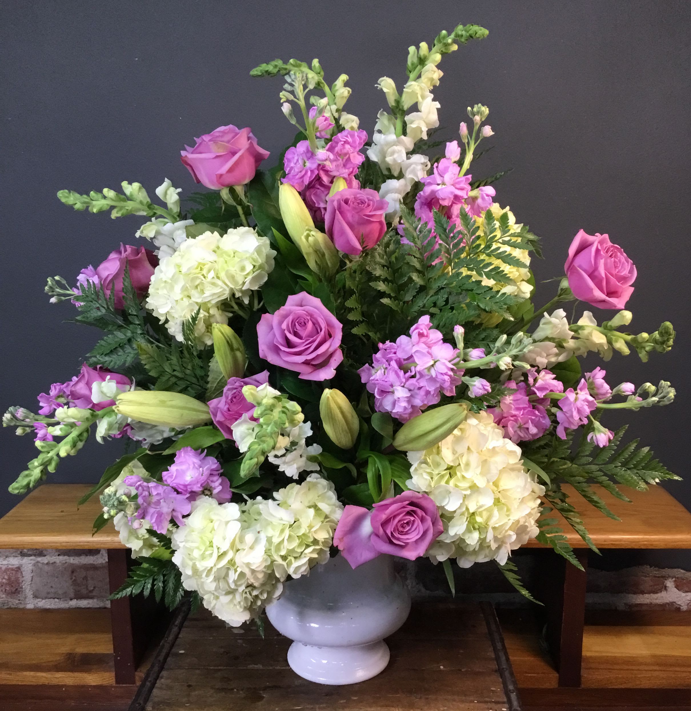 Lavendar and White Pot arrangment - Soft purple roses, creamy white hydrangeas, white lilies, and delicate lavender stock combine in a lavender and white flower arrangement perfect for an anniversary bouquet, wedding centerpiece, or a thoughtful sympathy display. The rounded white ceramic vase and the soft garden-inspired palette give the person you're thinking of an immediate sense of calm and classic elegance-the kind of arrangement that reads as both heartfelt and refined. 