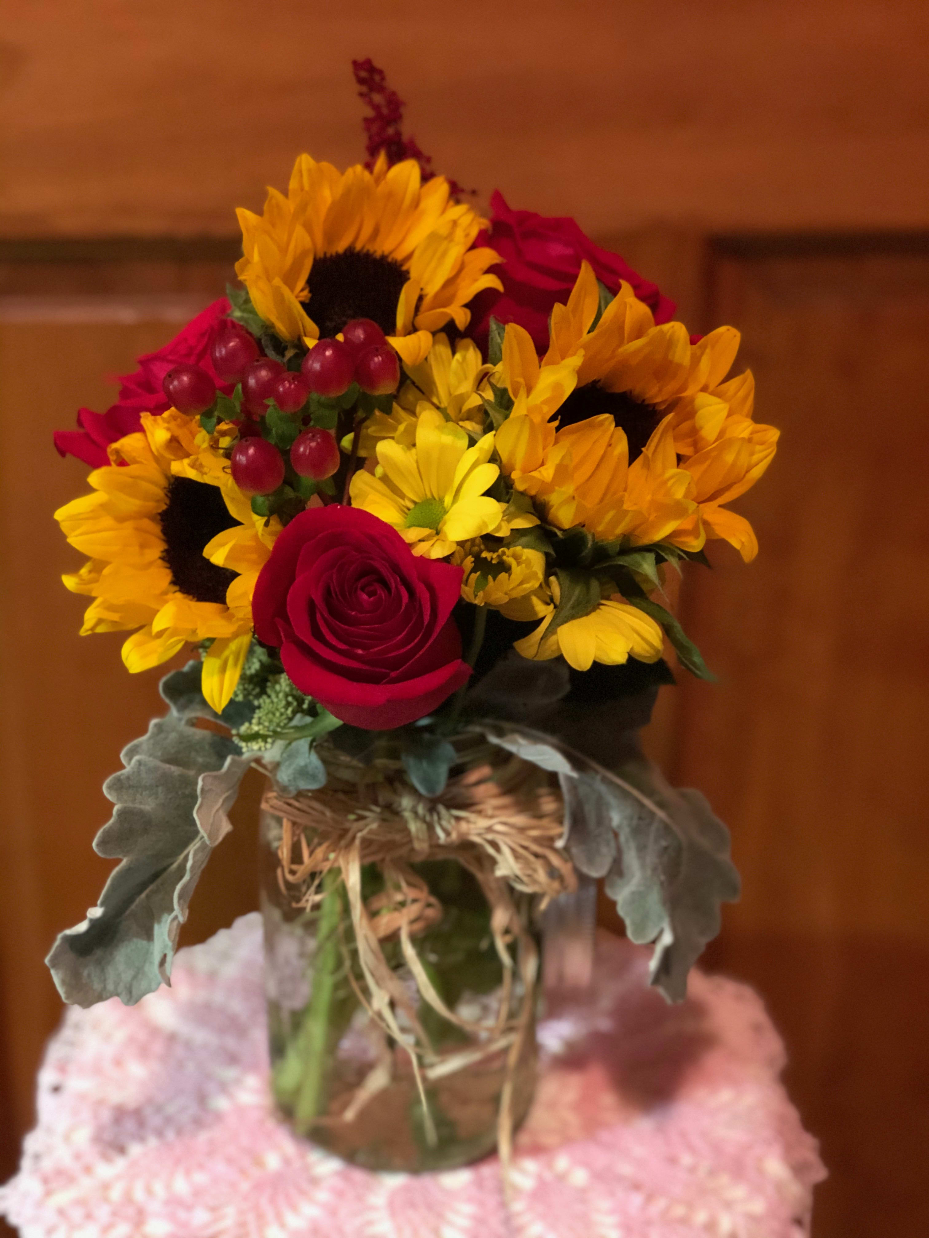 Bouquet of sunflowers and red roses in a glass vase