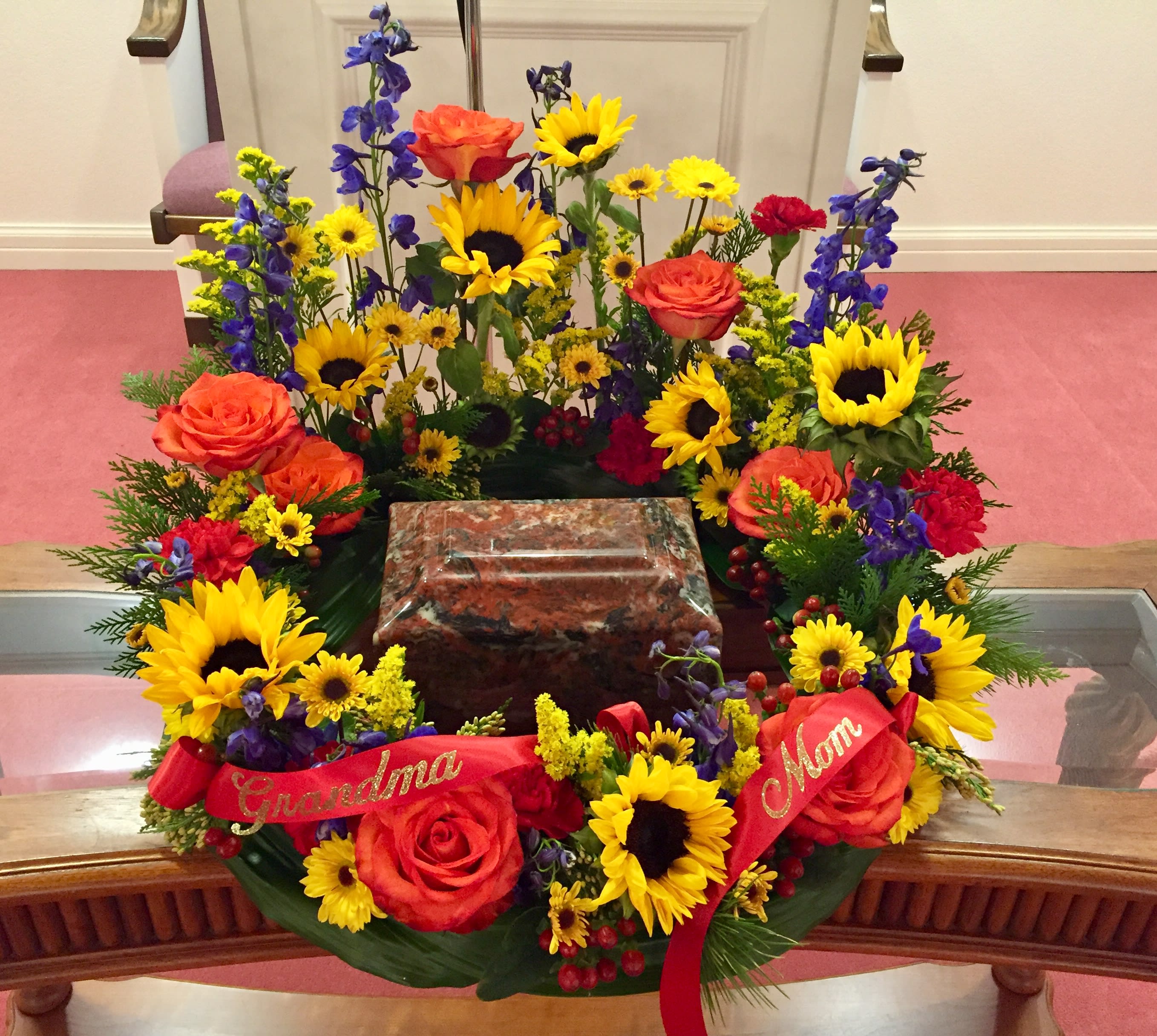 Colorful floral wreath around a memorial urn with red ribbons