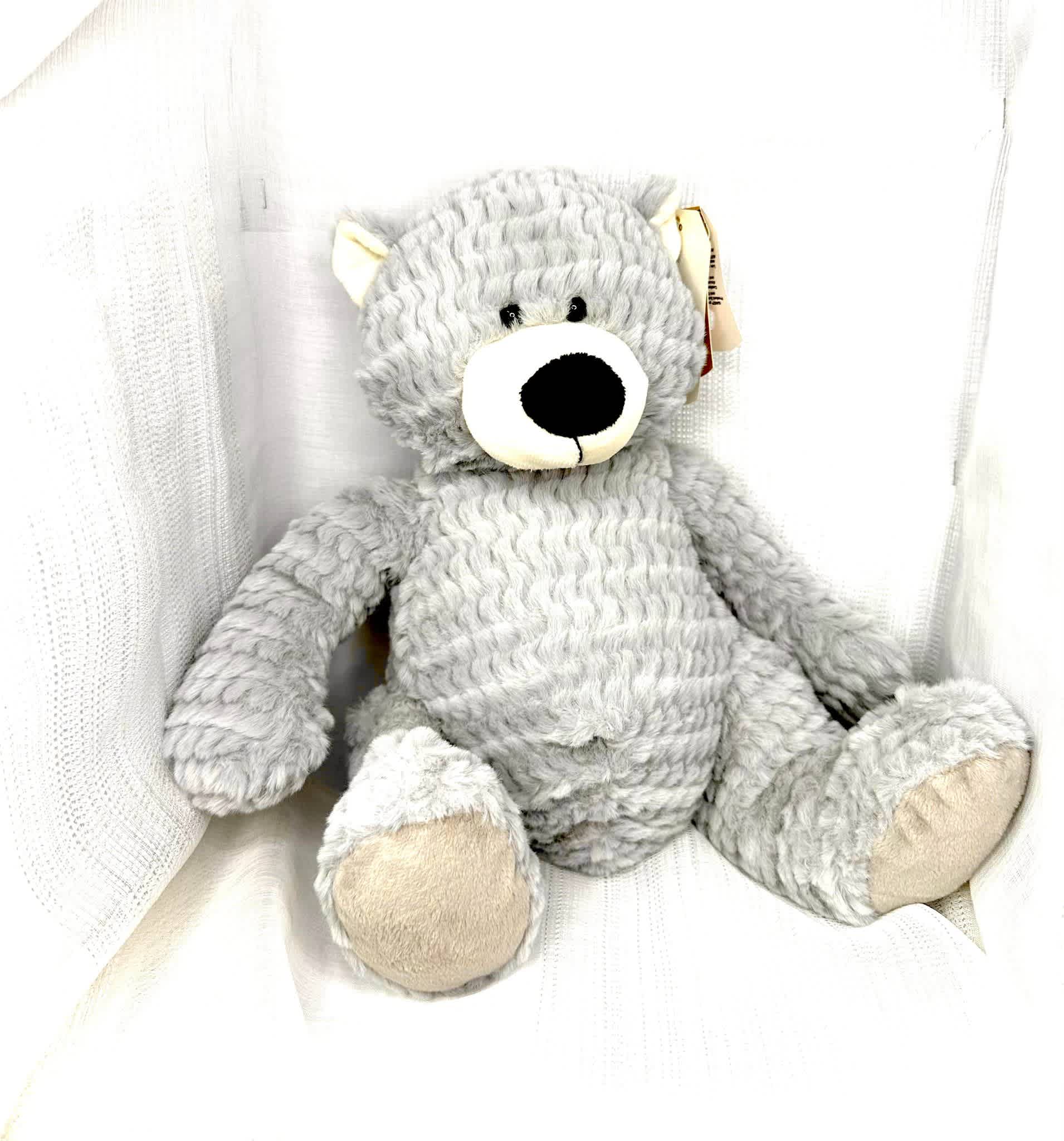Gray plush teddy bear sitting against white fabric