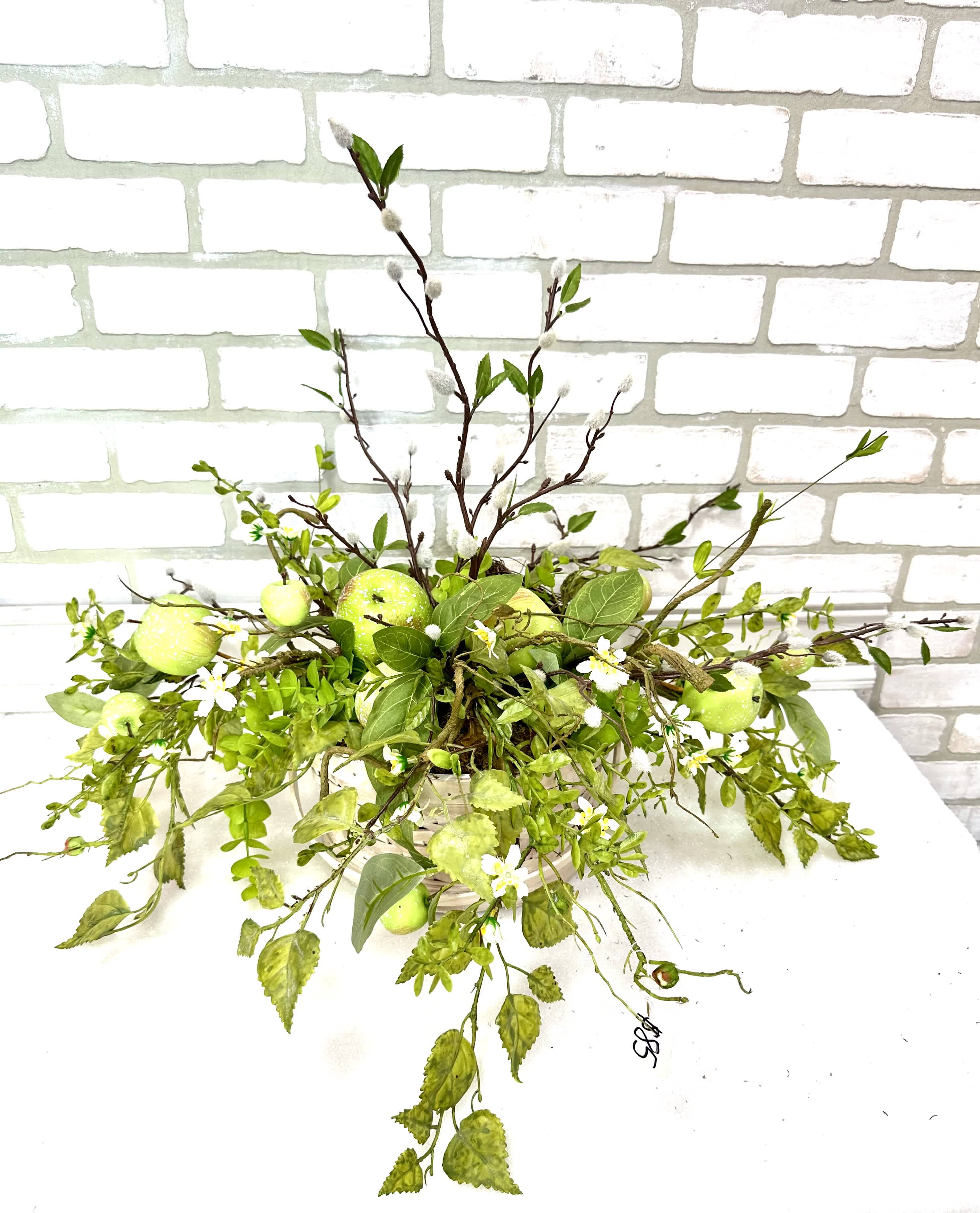 Green floral arrangement with apples in a low container