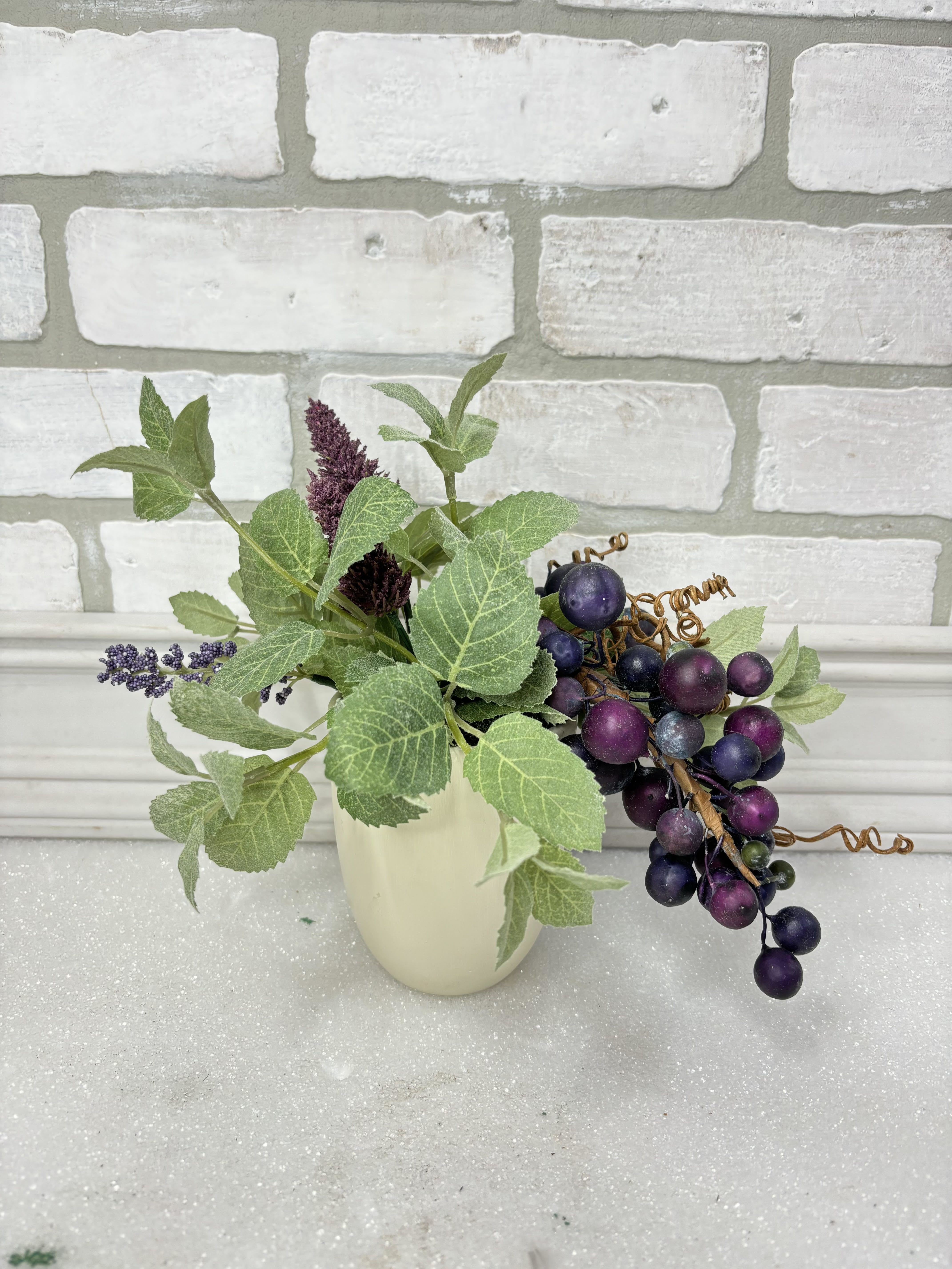 Small faux floral arrangement with purple berry clusters in a cream vase