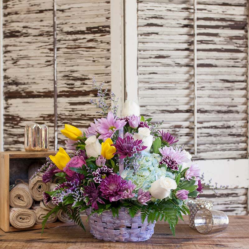 Basket arrangement of purple, yellow, white, and blue flowers
