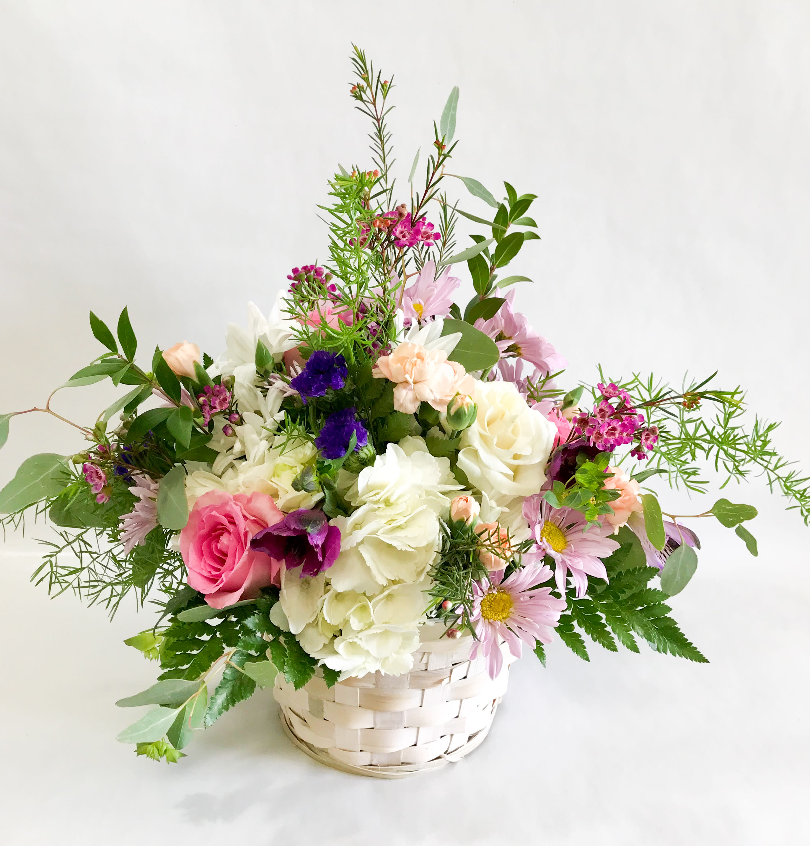 Mixed bouquet of pink, white, and purple flowers in a white basket