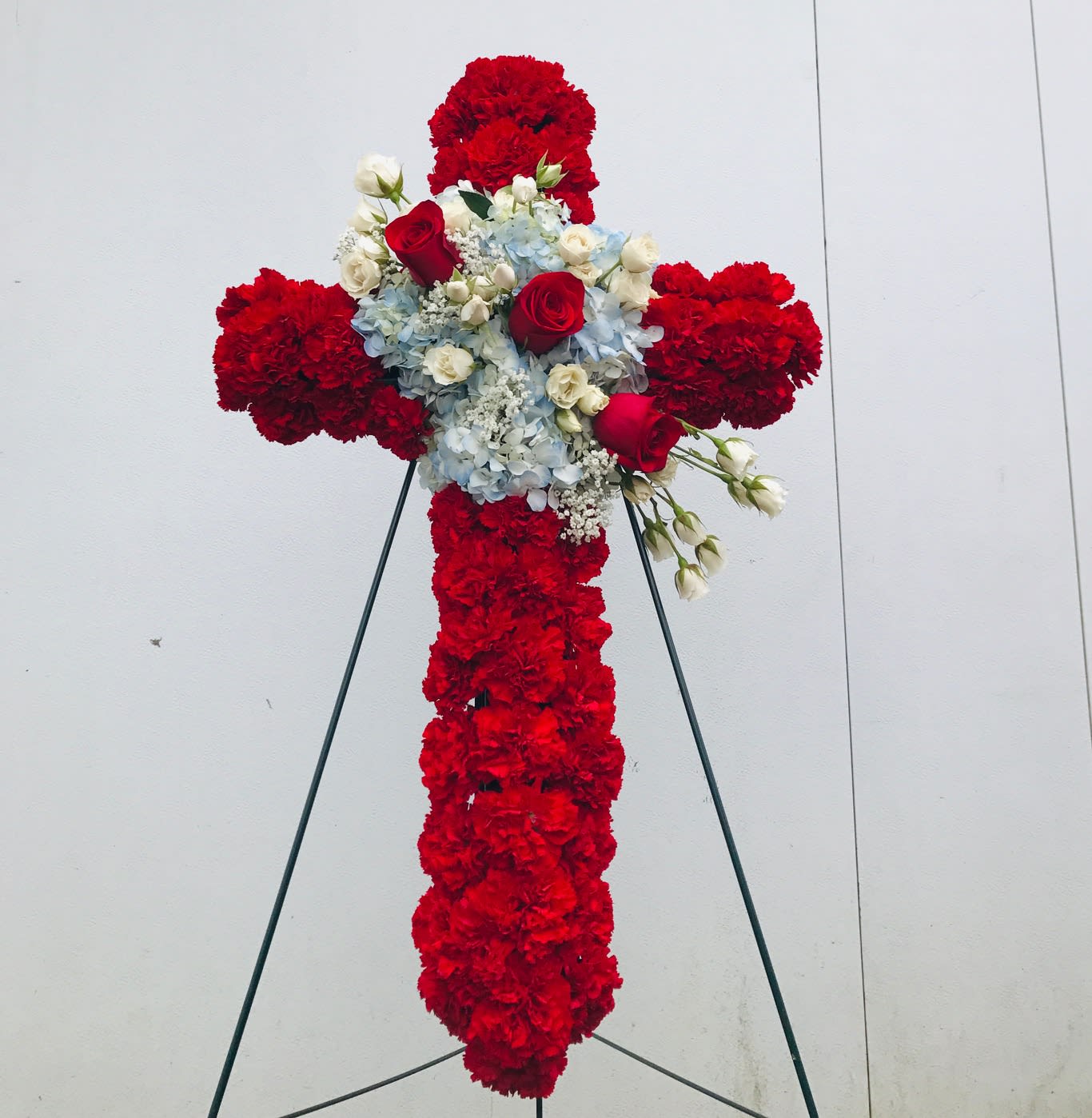 Red floral cross on a stand with white and blue flowers