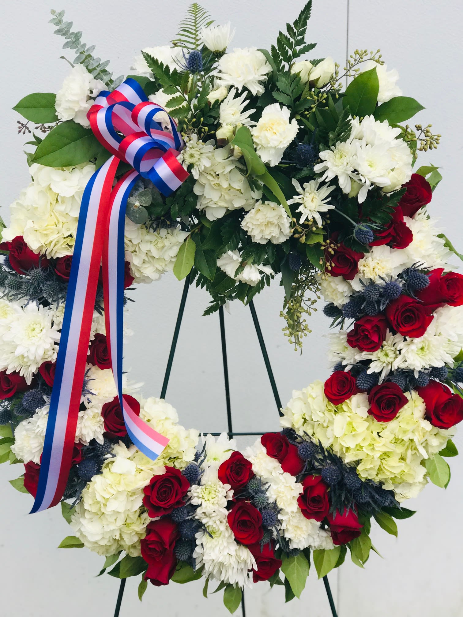 Floral wreath with red and white flowers and a tricolor ribbon on a stand