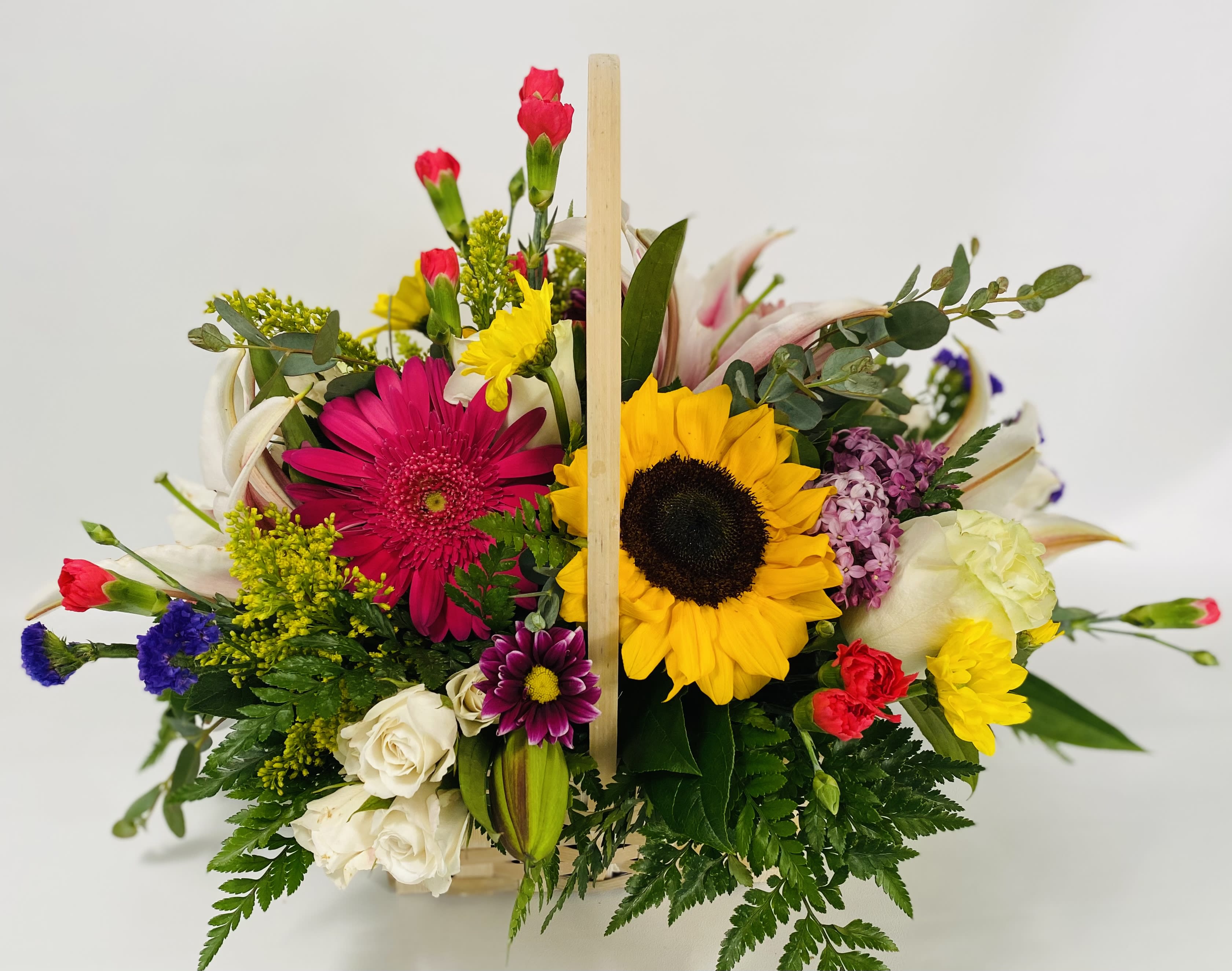 Mixed bouquet with sunflowers, gerbera daisies, roses, and carnations in a wooden basket