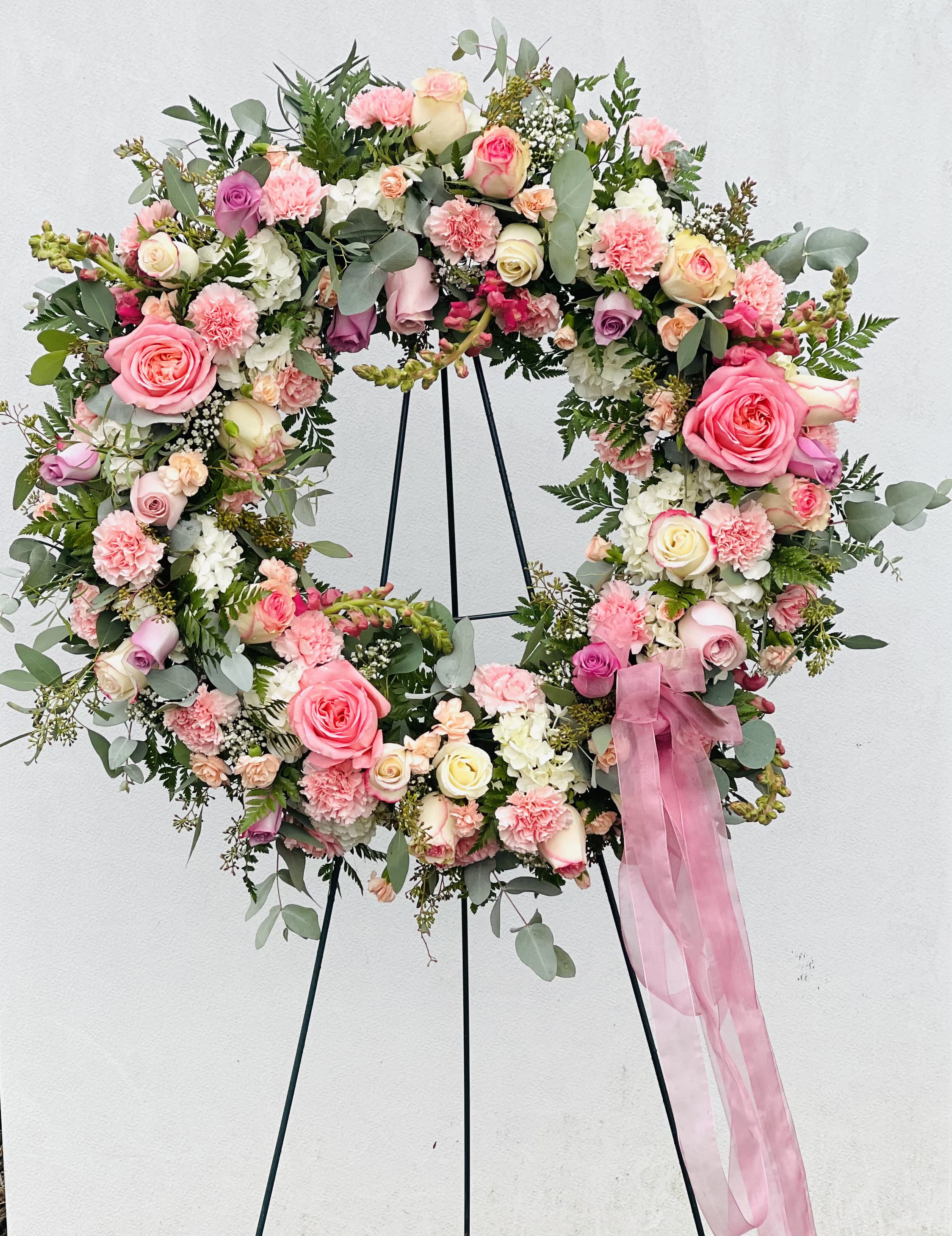 Heart-shaped floral wreath with pink and cream roses on a stand